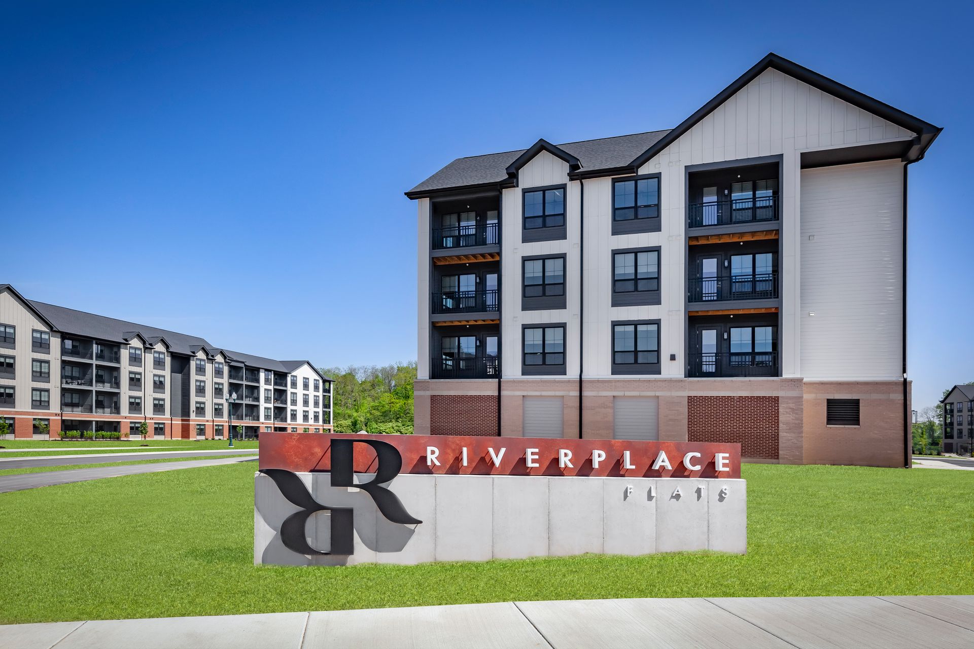 Sign for Riverplace Flats in front of a modern apartment building under a blue sky at River Place Flats in Fishers, IN.