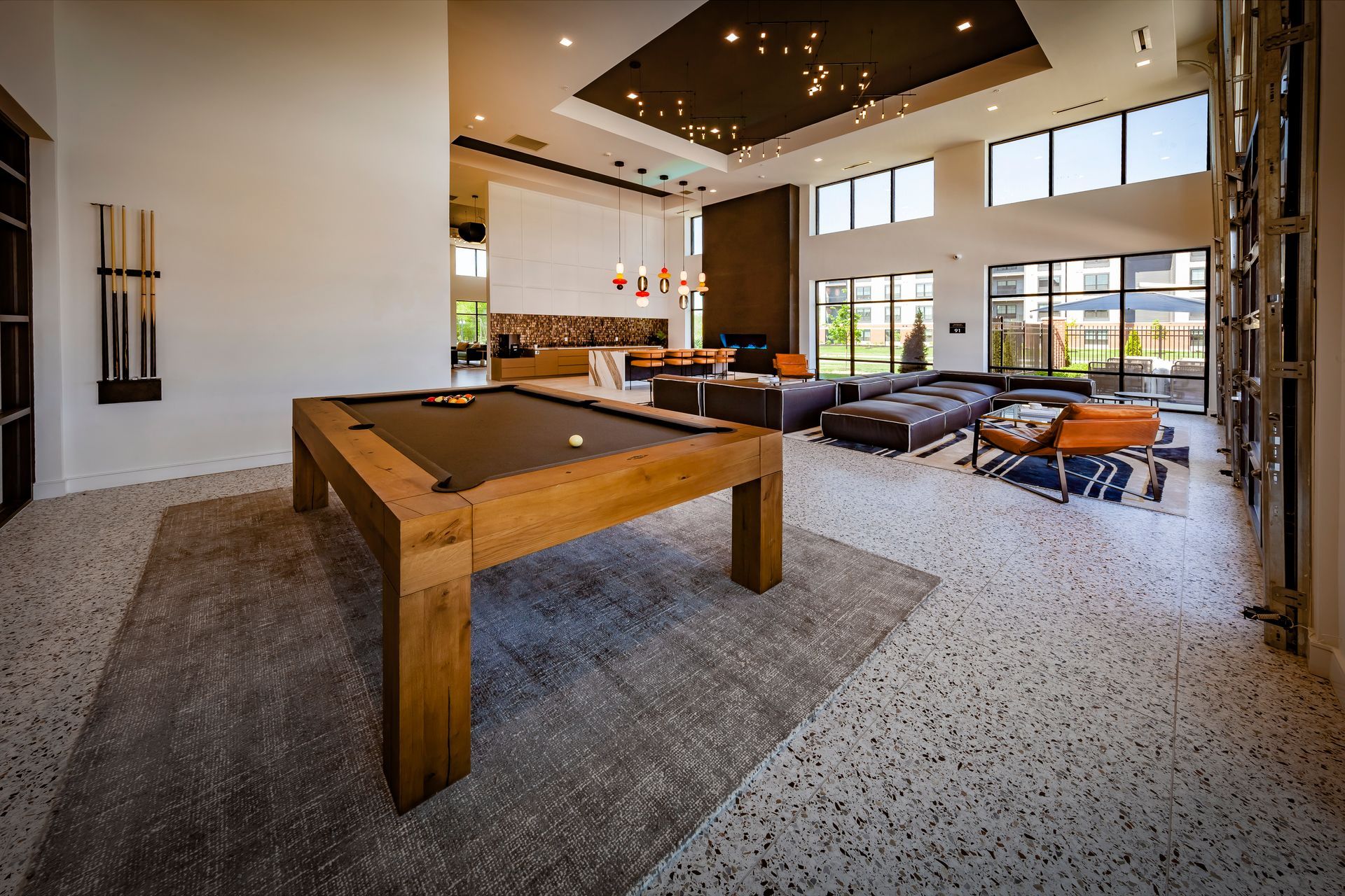 A modern lounge with a pool table, seating areas, and large windows; neutral colors dominate the space at River Place Flats in Fishers, IN.