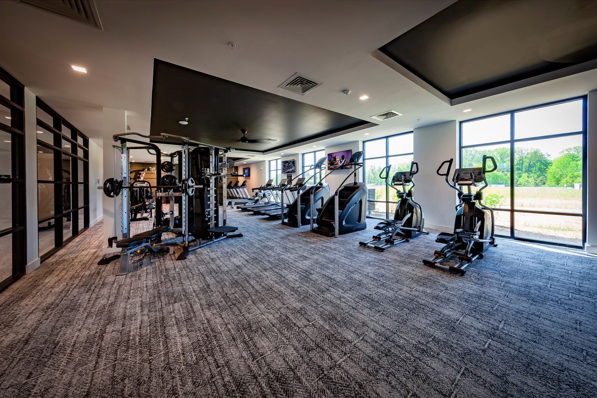 Gym interior with exercise equipment, cardio machines, and large windows overlooking green spaceat River Place Flats in Fishers, IN.