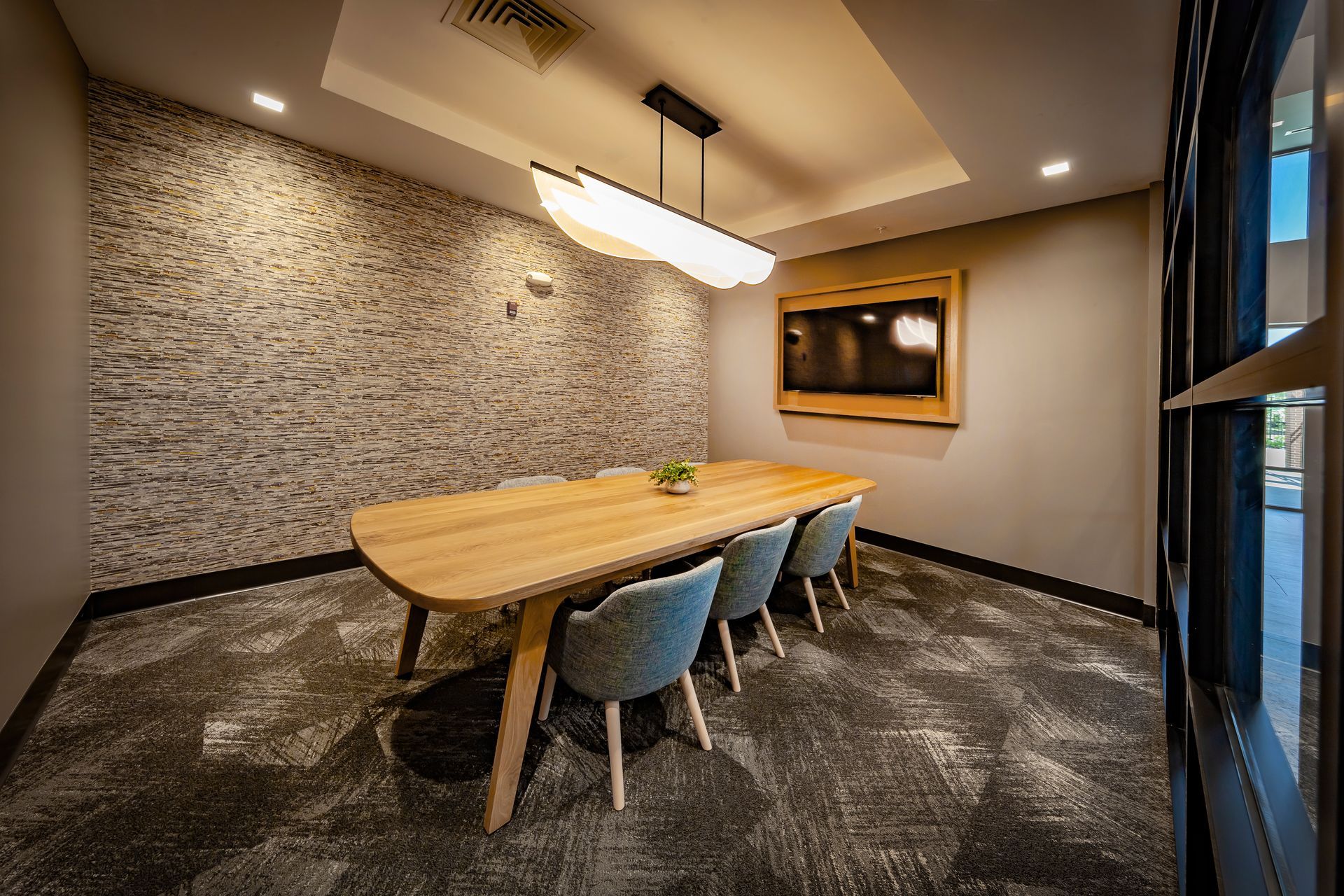 Conference room with a wooden table, blue chairs, and a TV on the wall at River Place Flats in Fishers, IN.