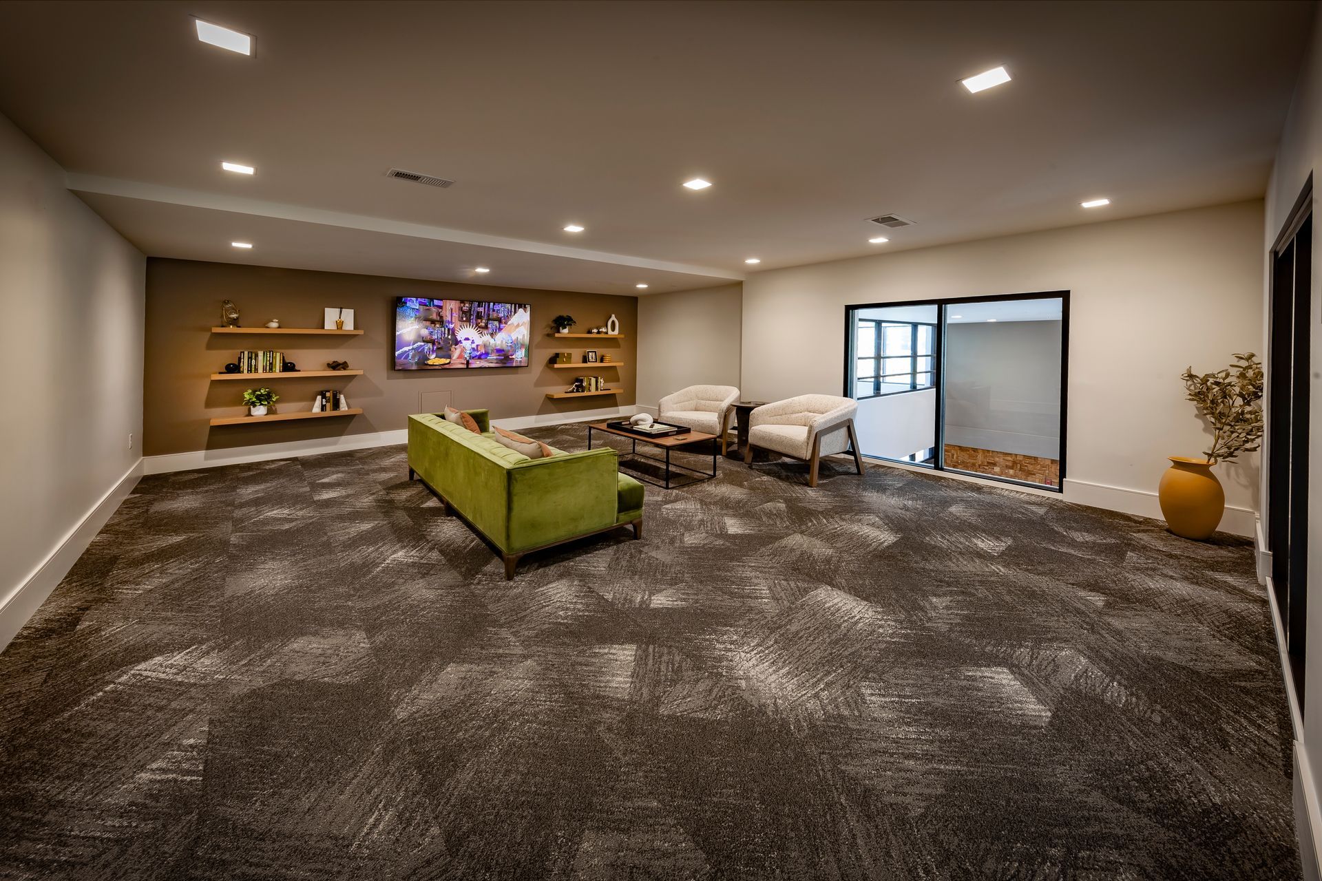 A modern waiting room with a green couch, two armchairs, and a television at River Place Flats in Fishers, IN.