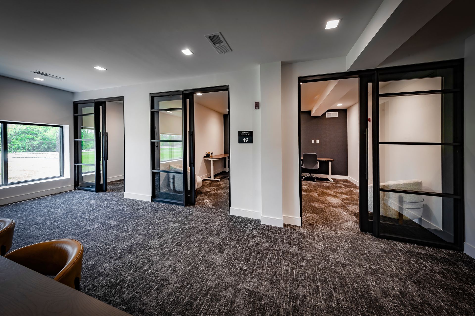Open office space with three glass-doored rooms, gray walls, and patterned carpet at River Place Flats in Fishers, IN.