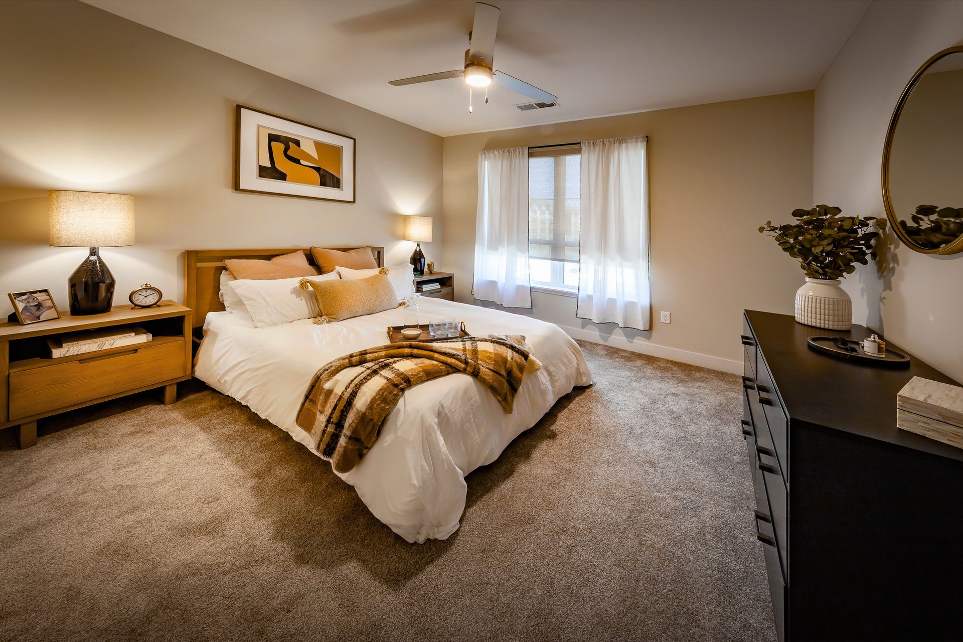 Bedroom with a wooden bed, beige walls, and a brown and white patterned blanket at River Place Flats in Fishers, IN.