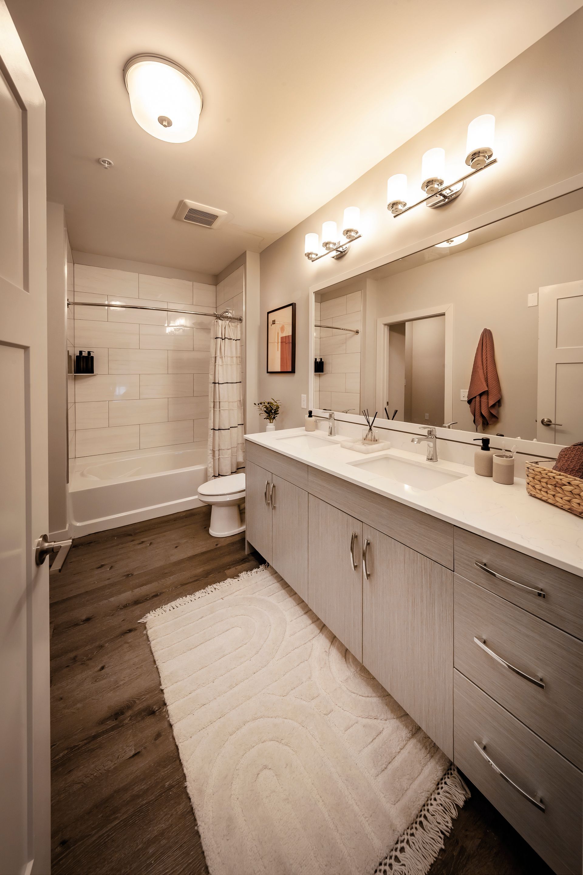 Modern bathroom with a white vanity, wooden floor, and a white rug at River Place Flats in Fishers, IN.
