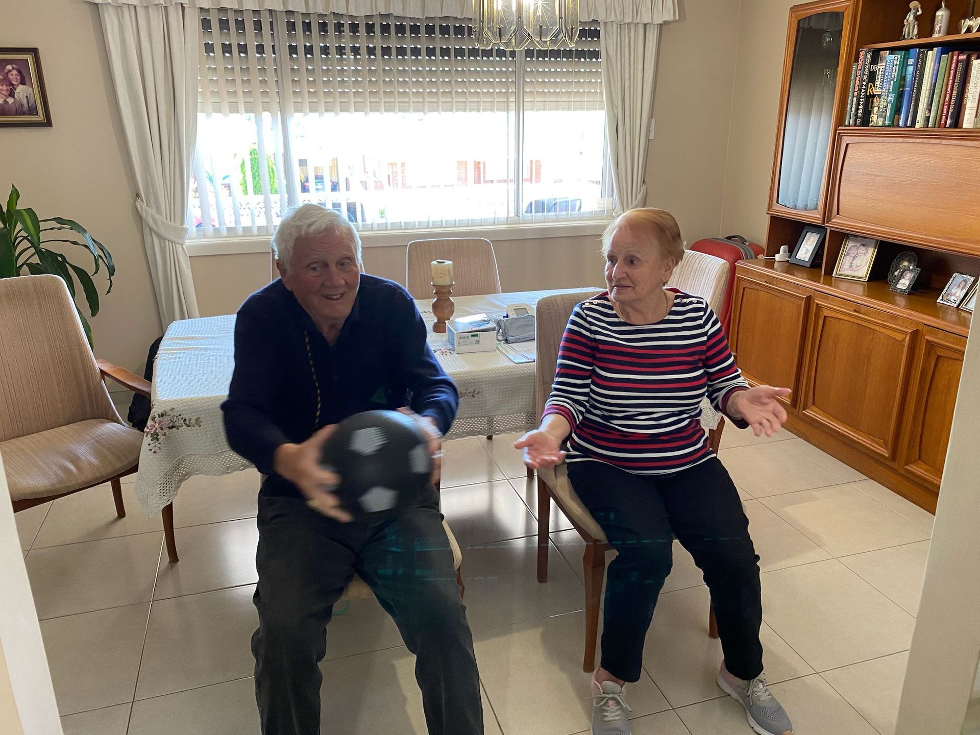 A man and a woman are sitting in a living room holding a soccer ball.