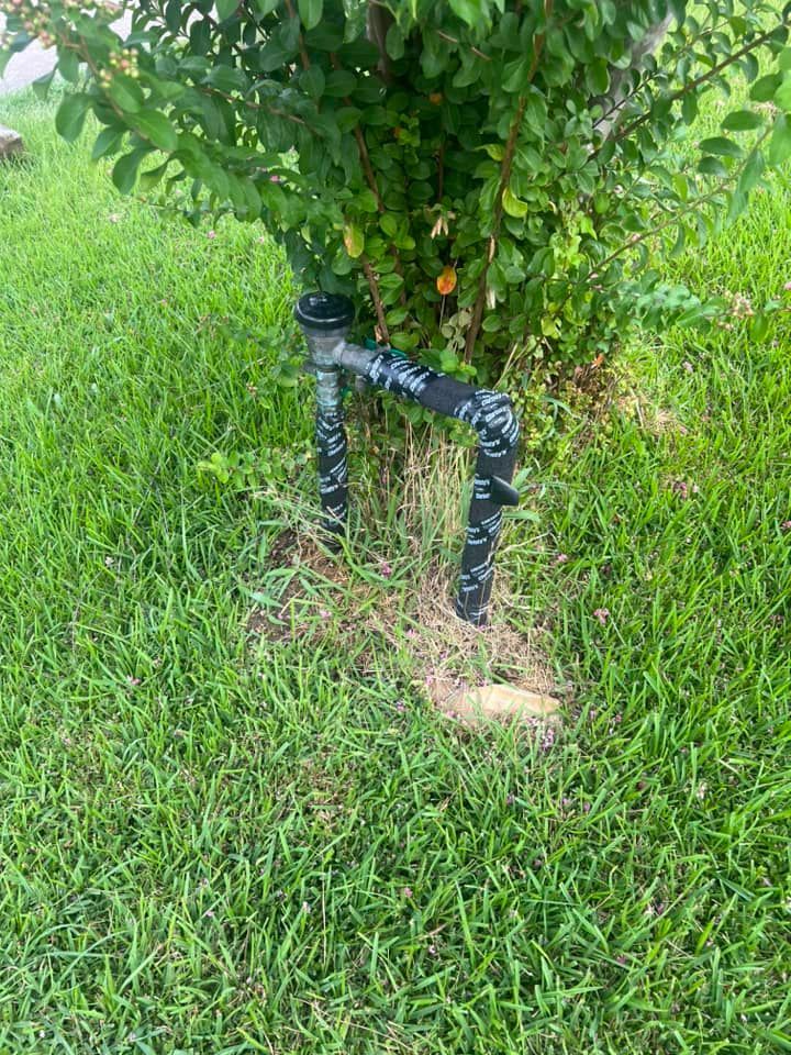 A black pipe is sitting in the grass next to a tree.