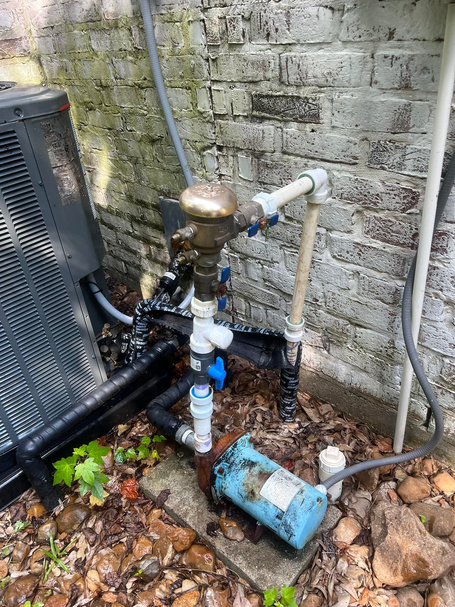 A water pump is sitting next to a brick wall.
