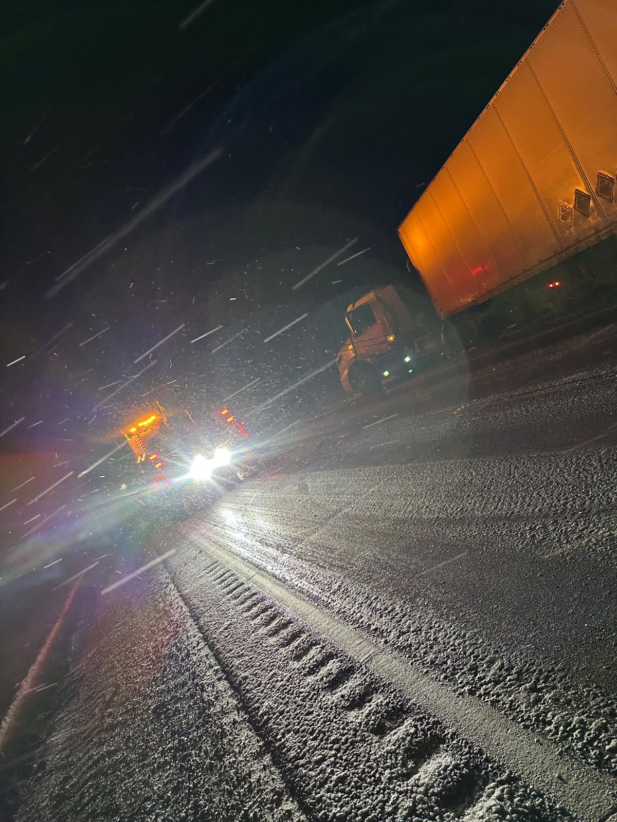 Snowy road at night, headlights illuminating, truck and semi-trailer.