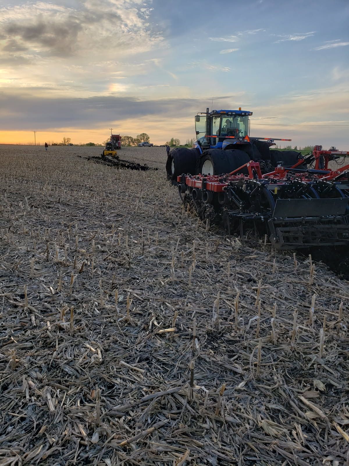 Tractor plowing a field at sunset. A second tractor is further in the field.