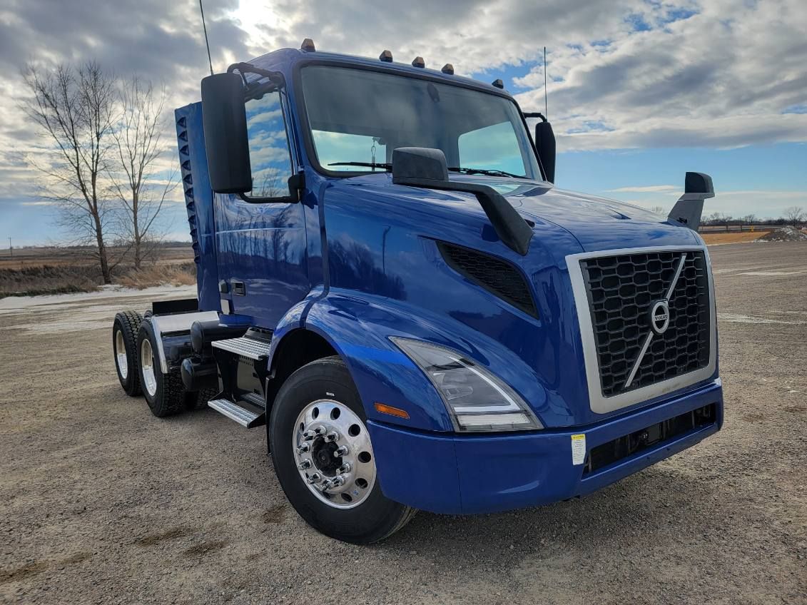 Blue Volvo semi-truck parked outdoors on gravel with cloudy sky background.