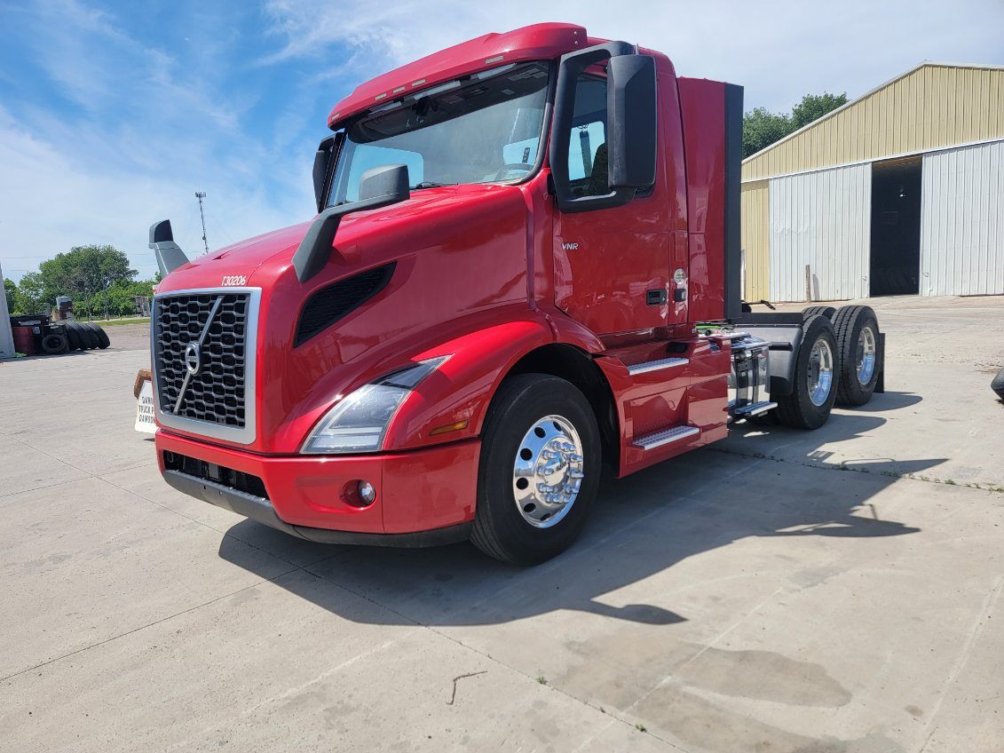 Red Volvo semi-truck parked on concrete lot under blue sky.