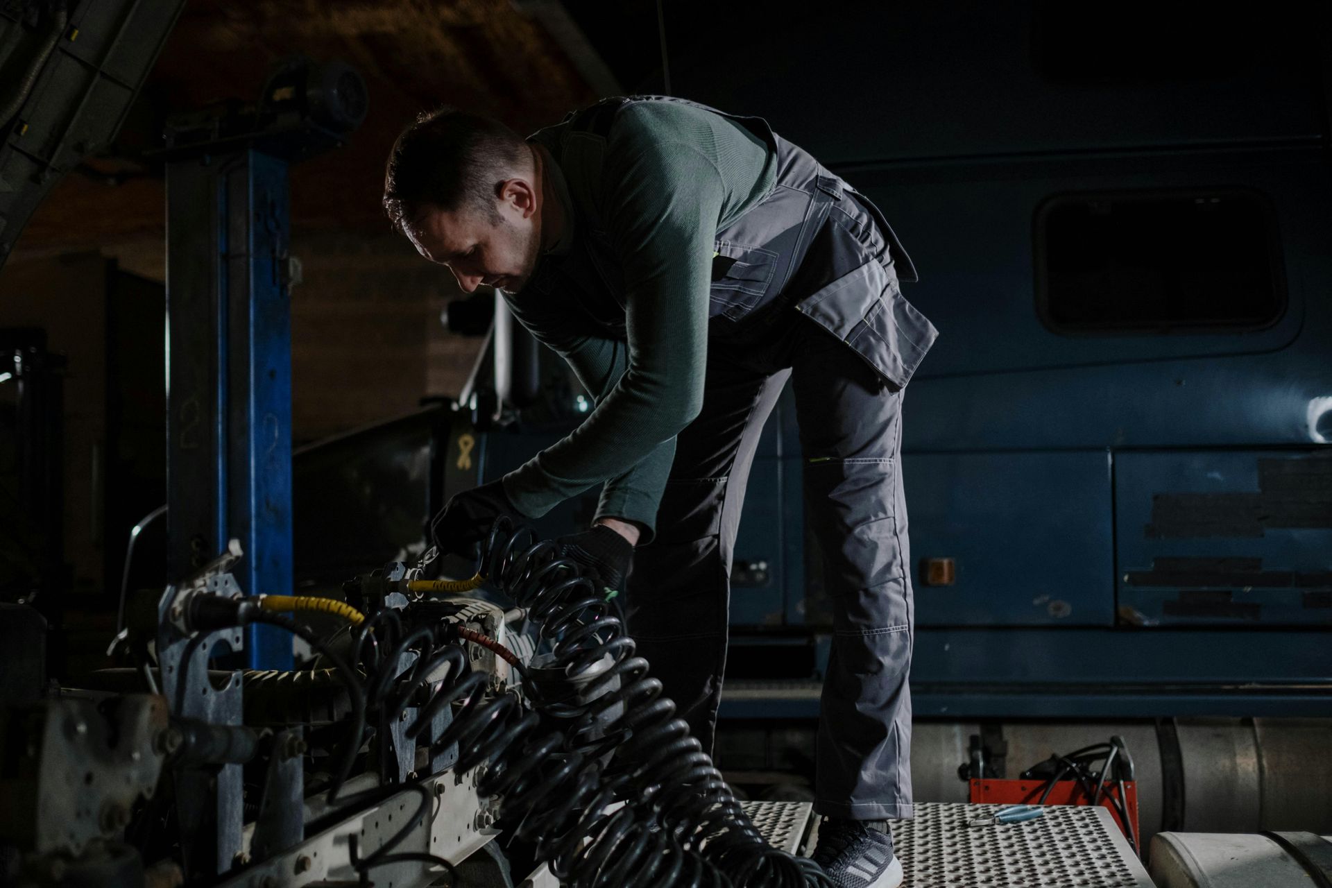 Mechanic in overalls inspecting engine in a dimly lit garage.