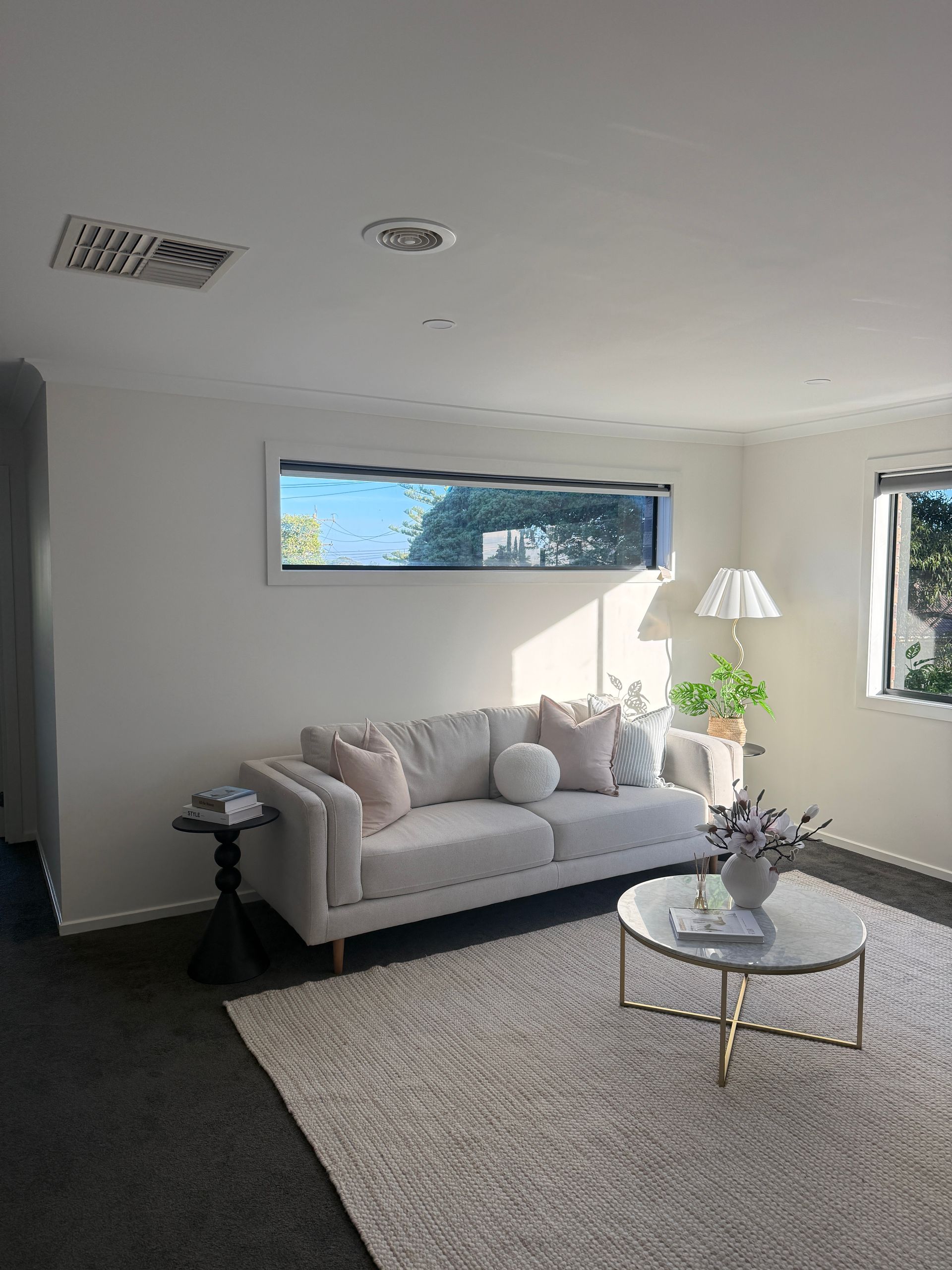 Bright living room with a white sofa, round coffee table, floor lamp, and sunlight through windows