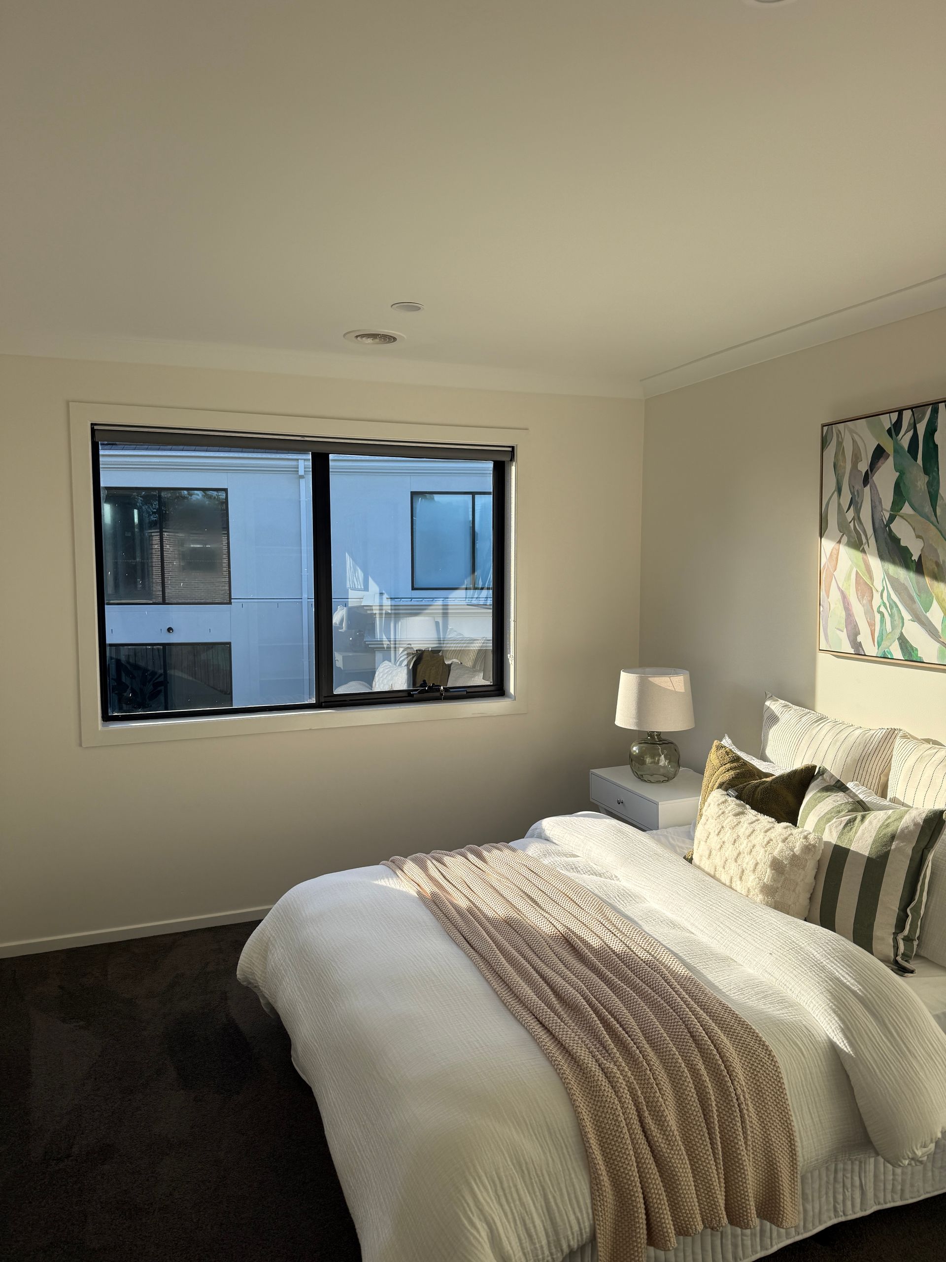 Bright bedroom with a bed, window, bedside lamp, and wall art
