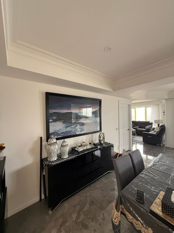 Dining room with black sideboard, wall art, and a set table leading into a bright living area.