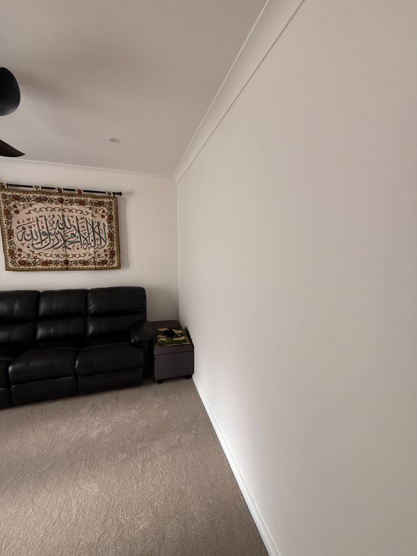 Empty beige room with black leather couch, small side table, and framed wall hanging