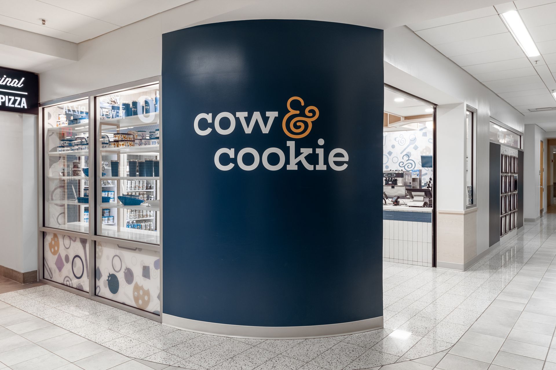 Penn State Cow & Cookie kiosk in a bright mall corridor with a dark blue curved sign and bakery display cases