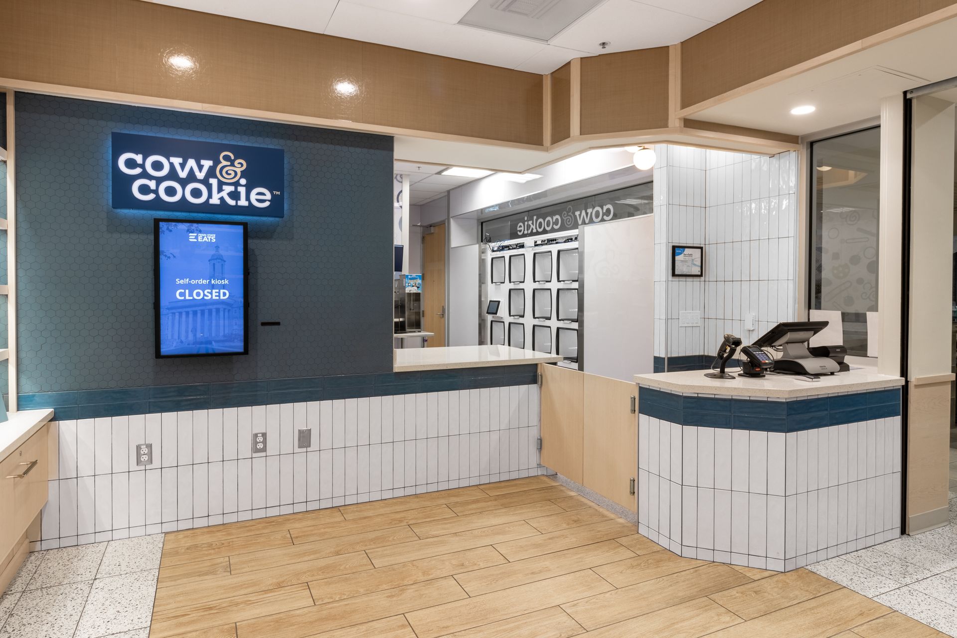 Penn State Cow & Cookie café counter with blue sign, white cabinetry, and wood flooring inside a modern shop