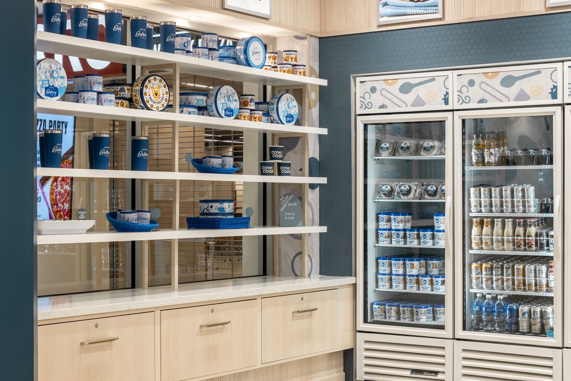 Penn State Cow & Cookie's store shelves with blue-and-white packaged goods and glass-door refrigerated coolers in a retail aisle