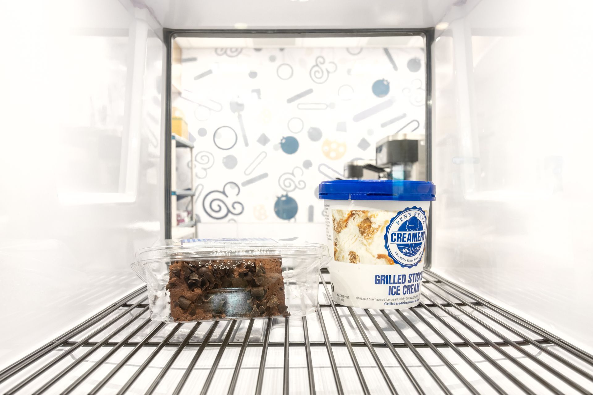 Penn State Cow & Cookie's inside a bright fridge, a blue-lidded jar sits beside a square food container on wire shelves.
