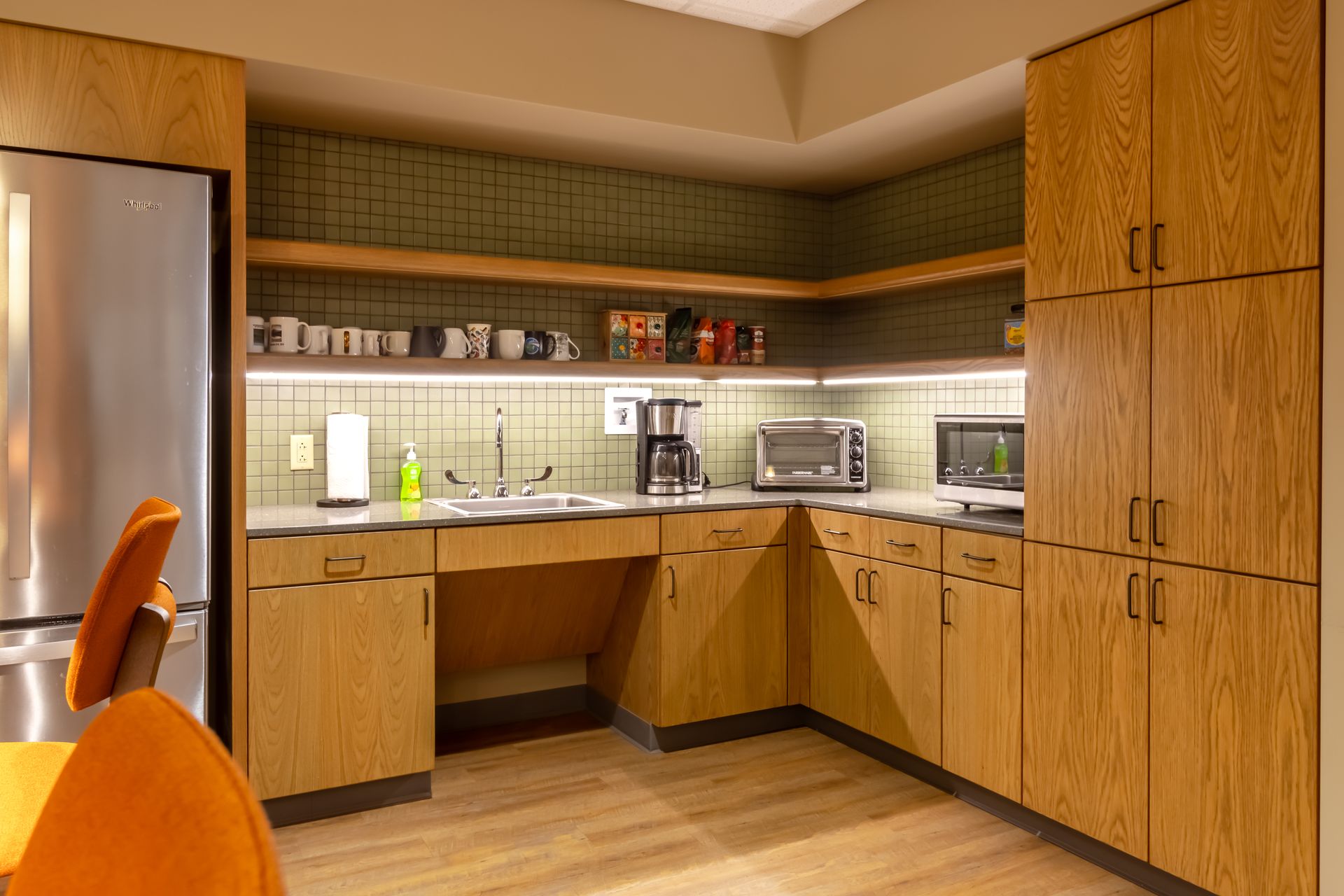 Penn State EESI Suite's modern kitchen with wood cabinets, stainless appliances, and an orange chair by the counter