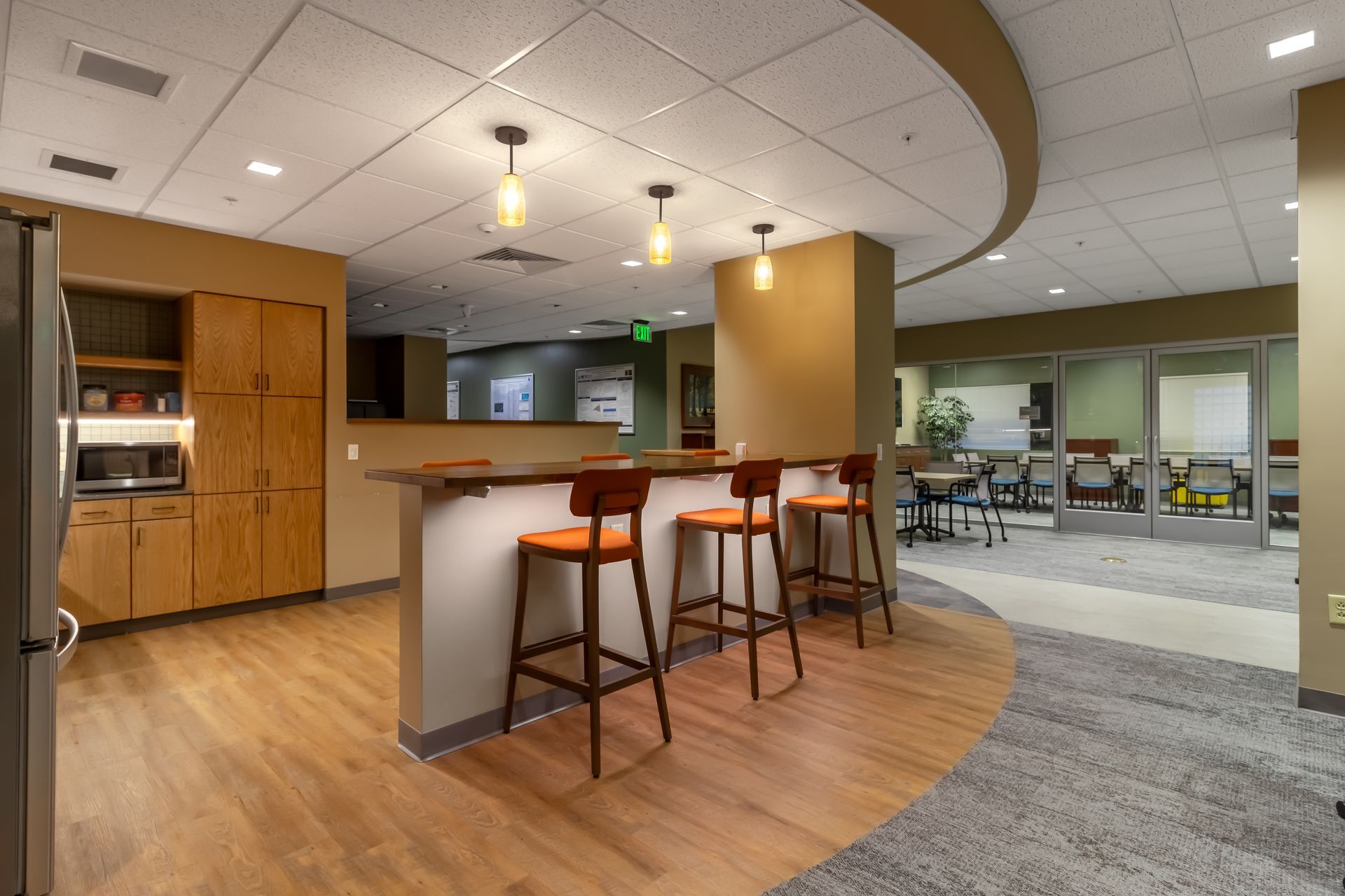 Penn State EESI Suite's modern office kitchenette with wood cabinets, island seating, and lounge area under pendant lights