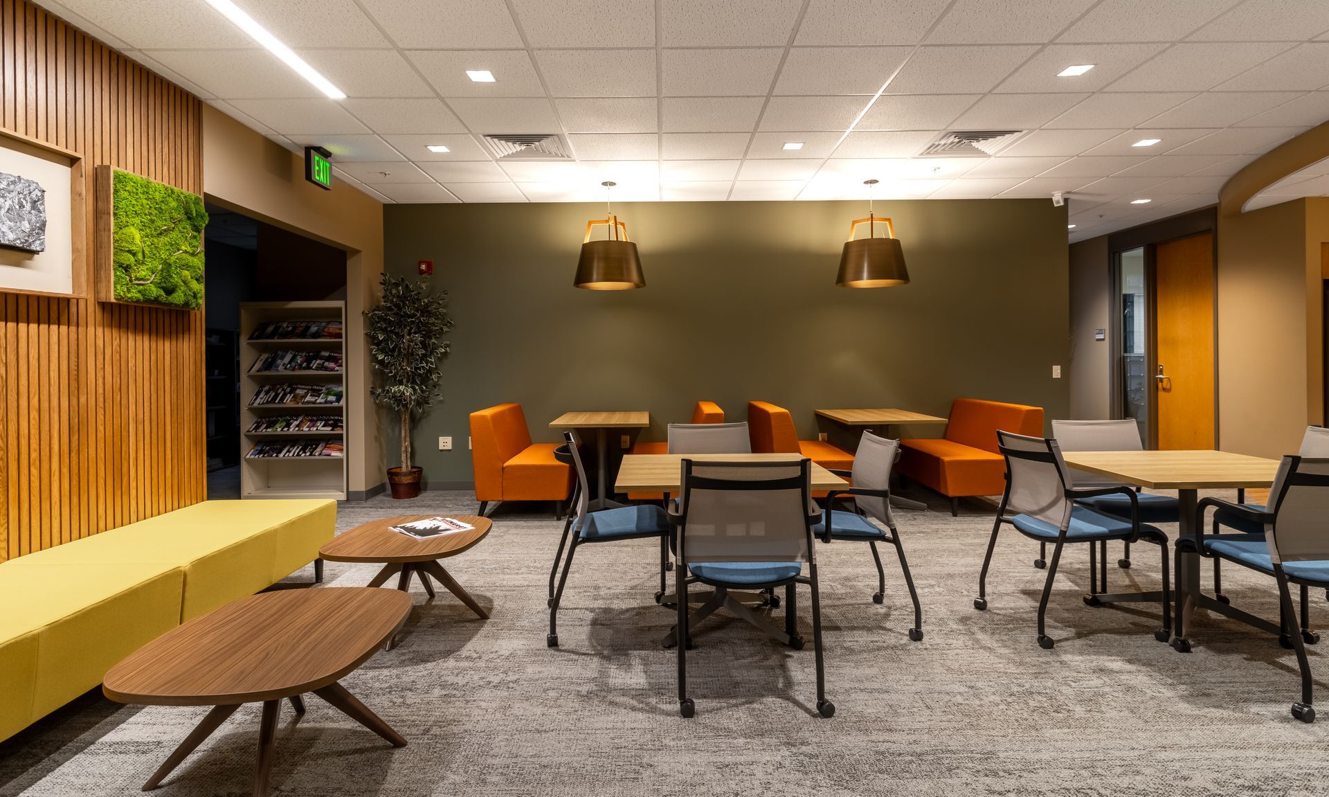 Penn State EESI Suite's modern lounge with small tables, orange chairs, carpet, and wall art under warm pendant lights