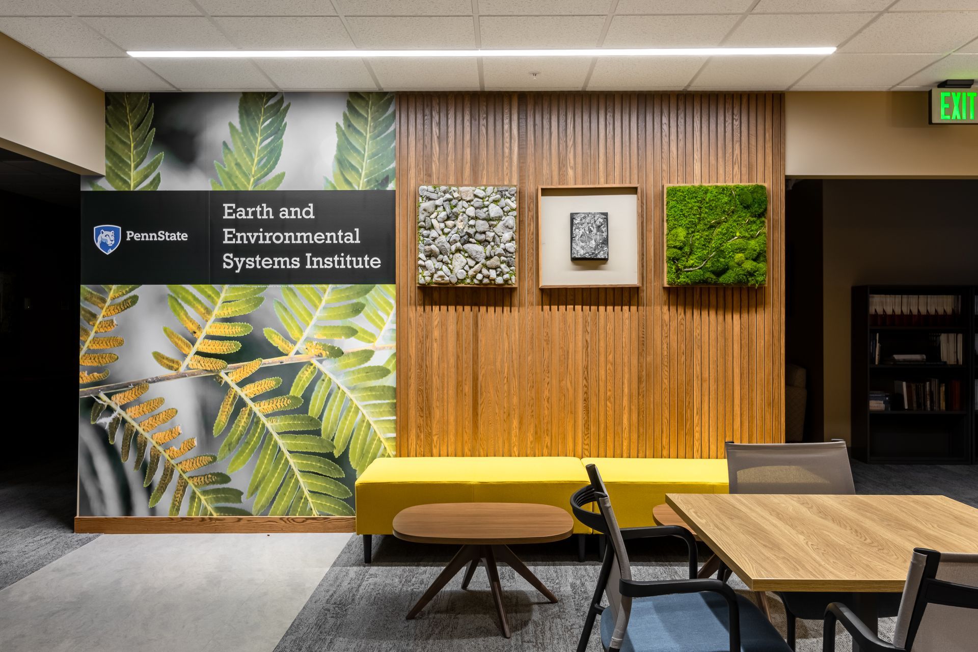 Penn State EESI Suite's modern lobby with wood slat wall, moss art panels, yellow bench, and tables and chairs.