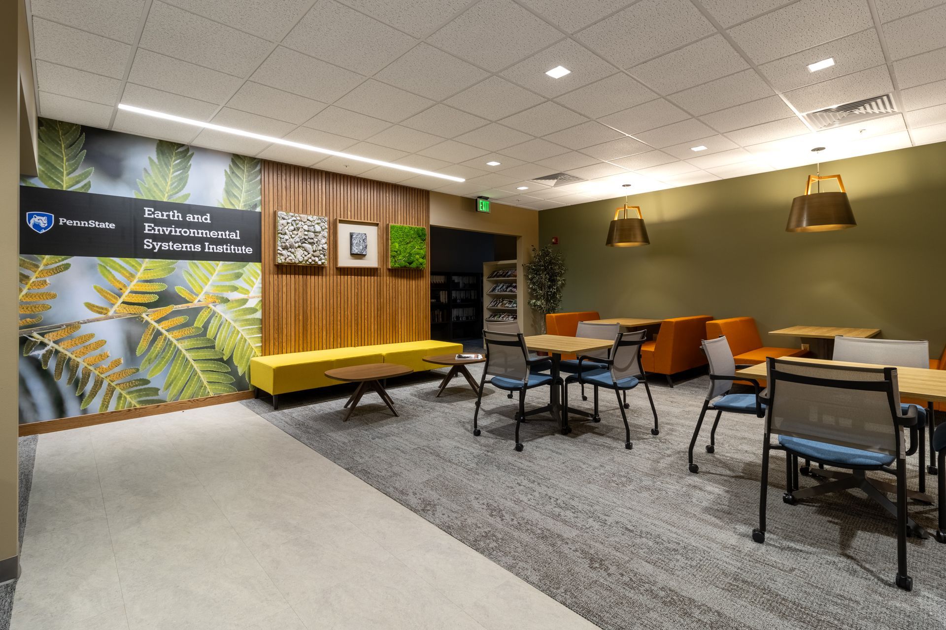 Penn State EESI Suite's modern lounge with colorful wall art, yellow bench, tables, and chairs under warm pendant lights.