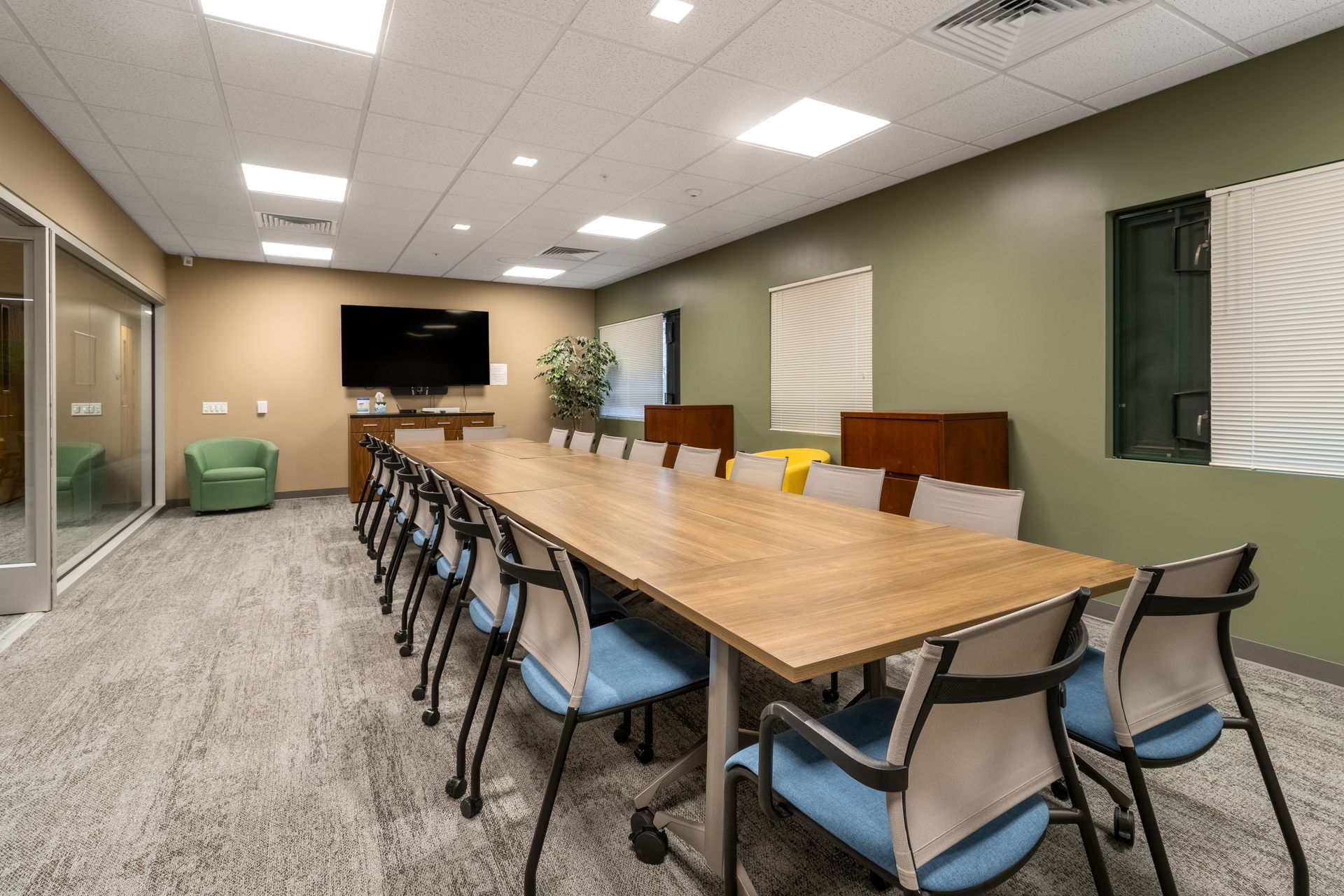 Penn State EESI Suite's conference room with long wooden table, chairs, wall-mounted TV, and green armchair on carpeted floor.