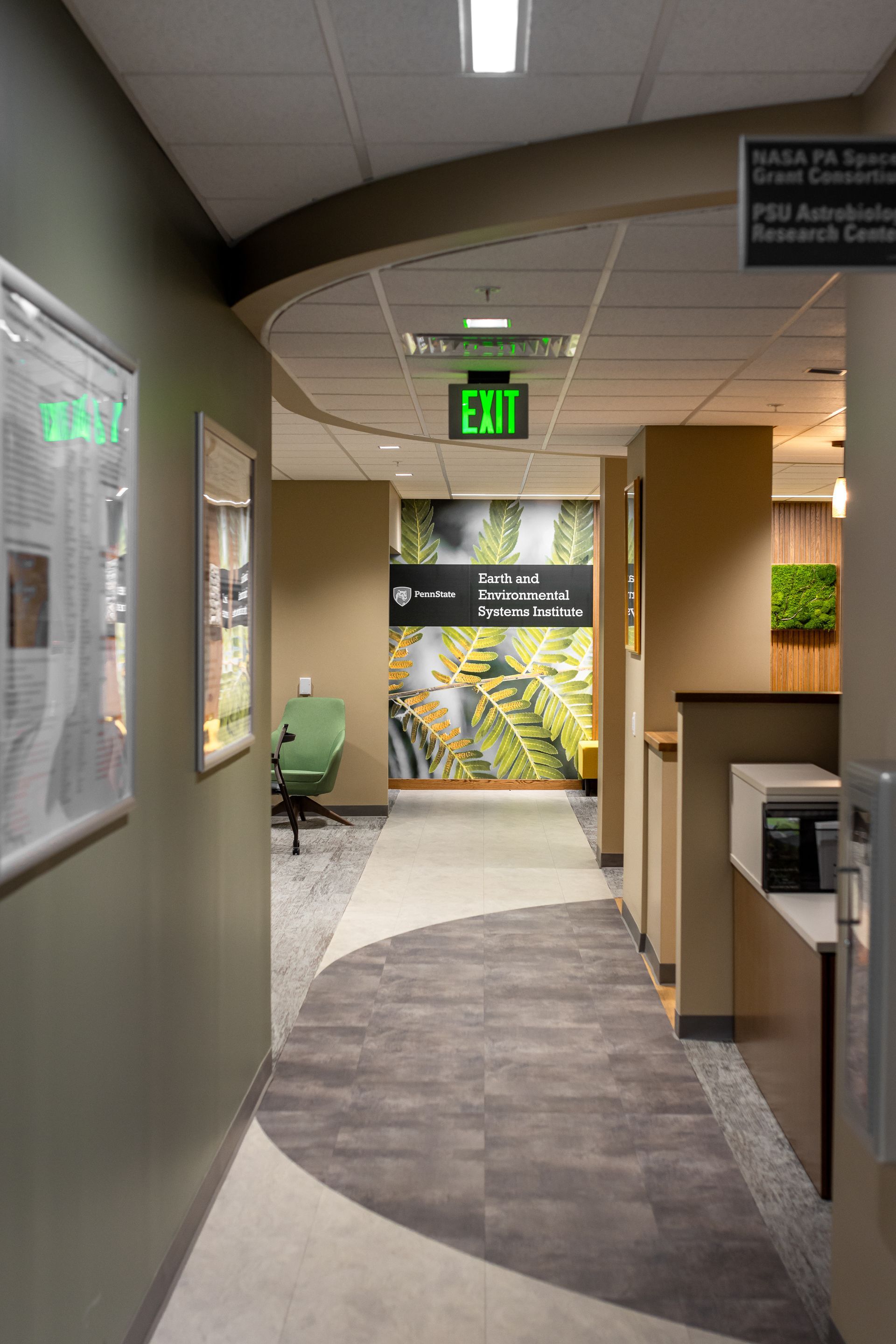 Office hallway with green exit signs, cubicles, and a curved carpeted walkway