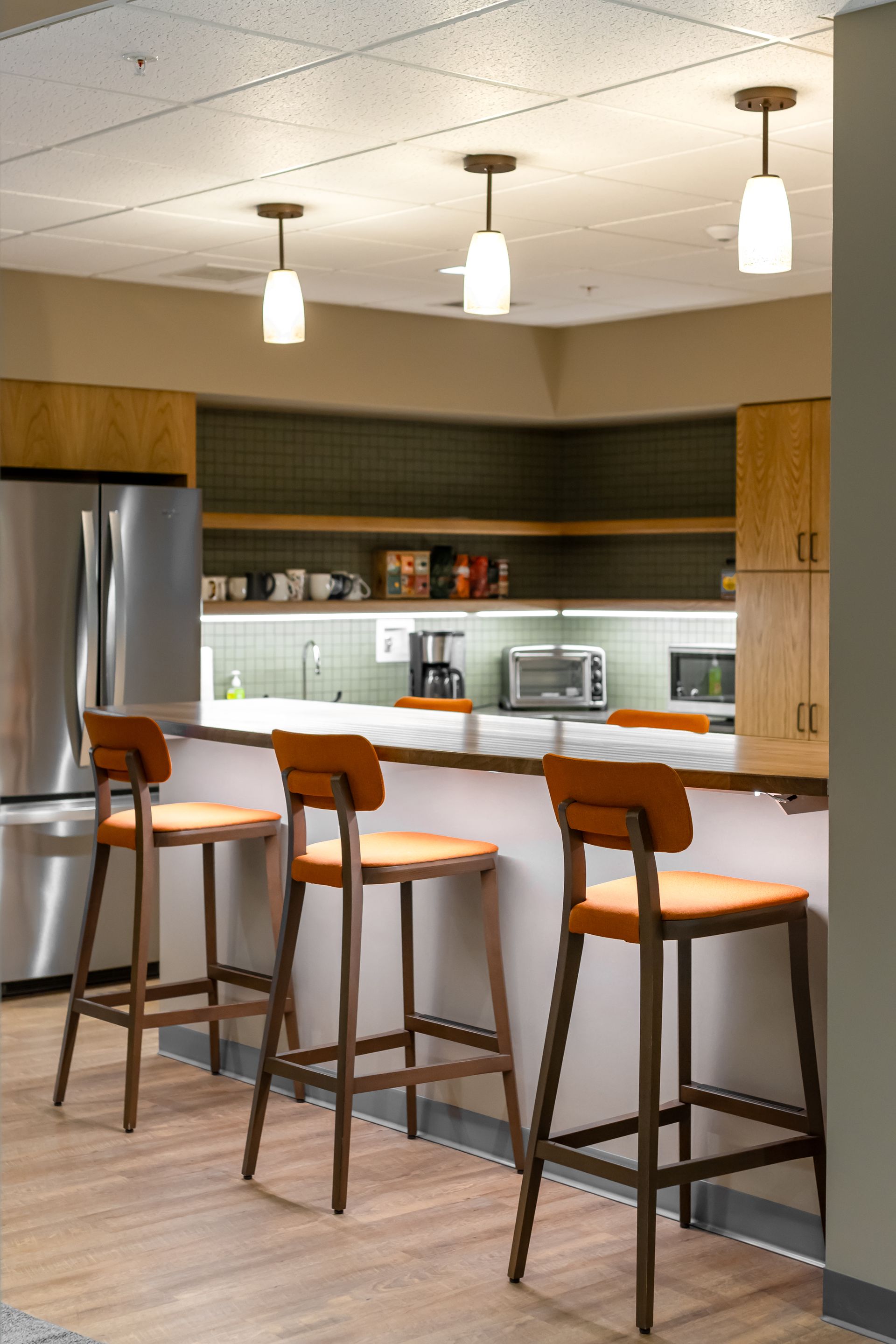 Penn State EESI Suite's modern kitchen with stainless steel fridge, island stools, and pendant lights