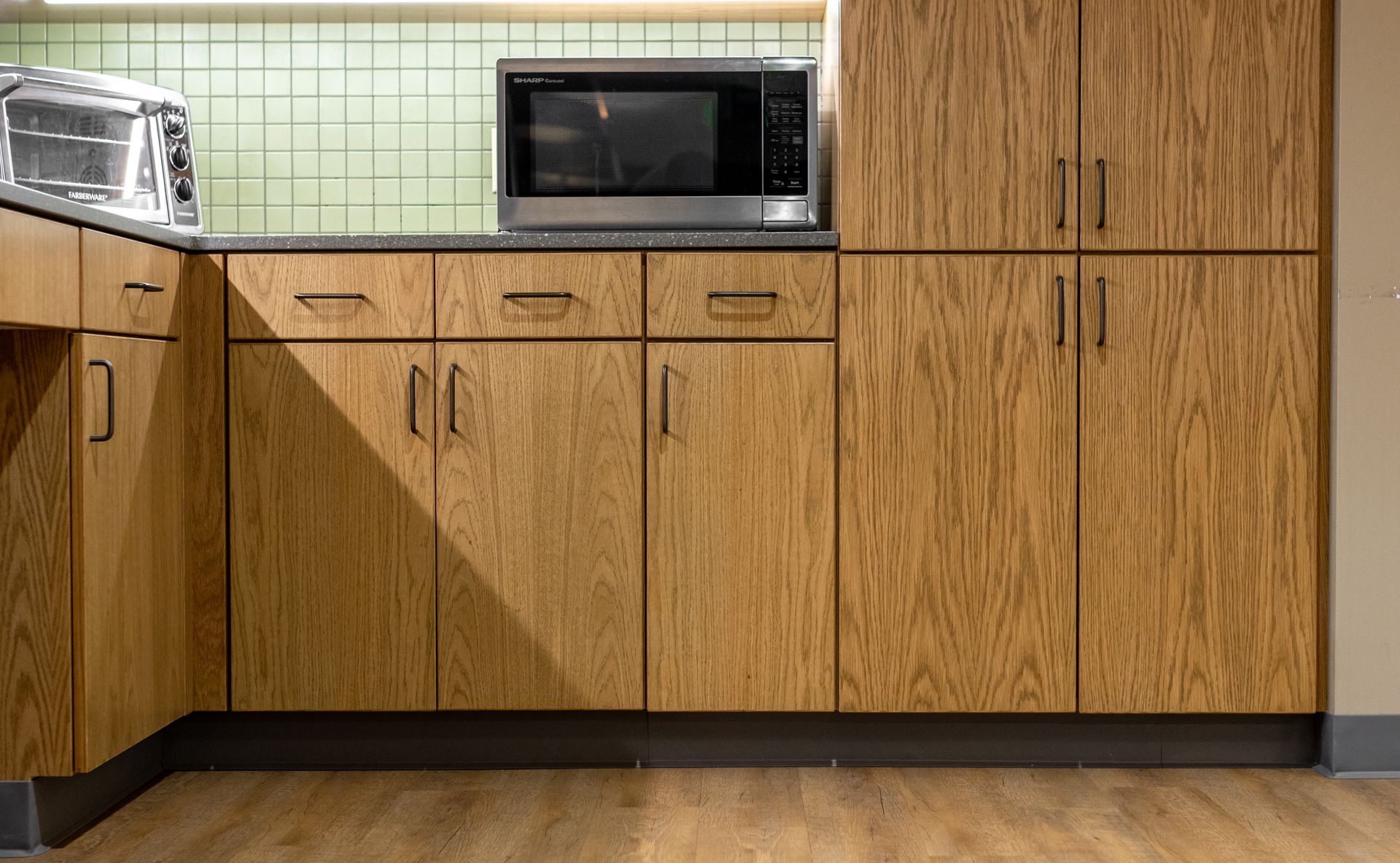 Penn State EESI Suite's modern kitchen with wood cabinets, green tile backsplash, microwave, and countertop appliances