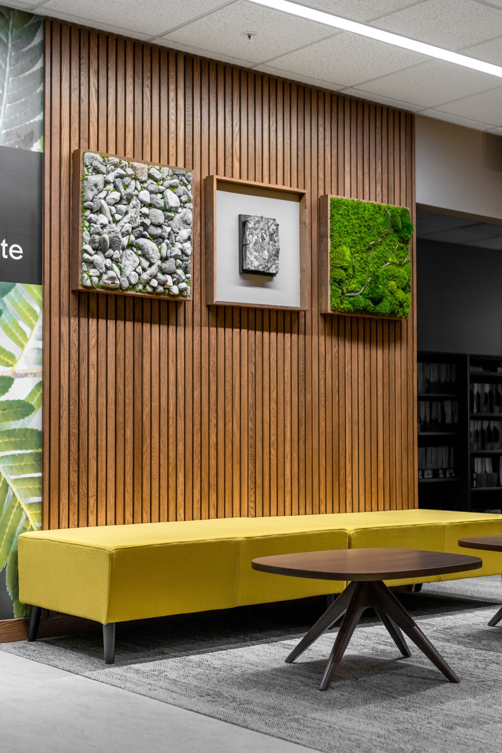 Penn State EESI Suite's modern lounge with yellow bench, round table, wood slat wall, and framed art and moss panels