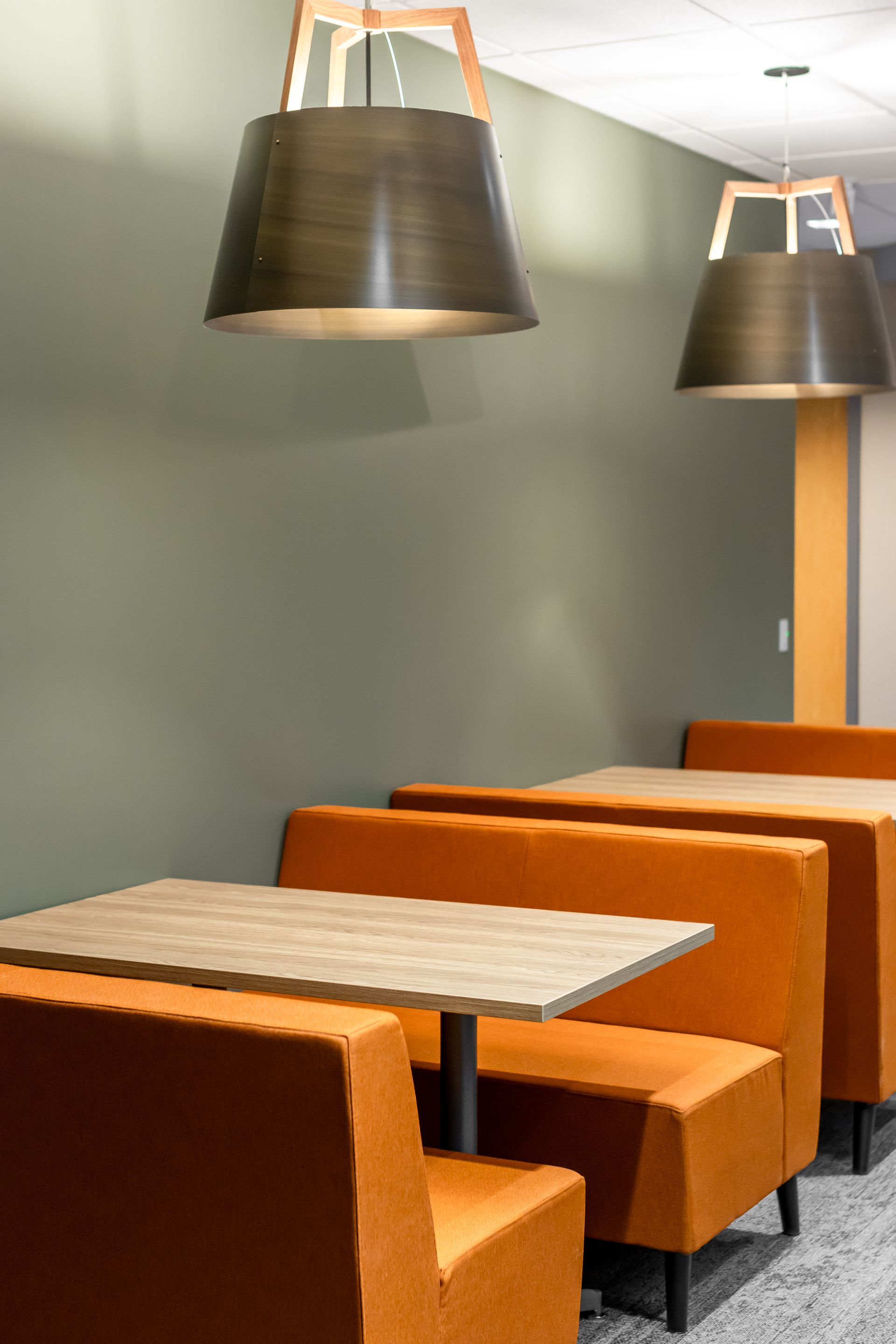 Penn State EESI Suite's modern café booth seating with orange chairs, wooden tables, and hanging black pendant lights