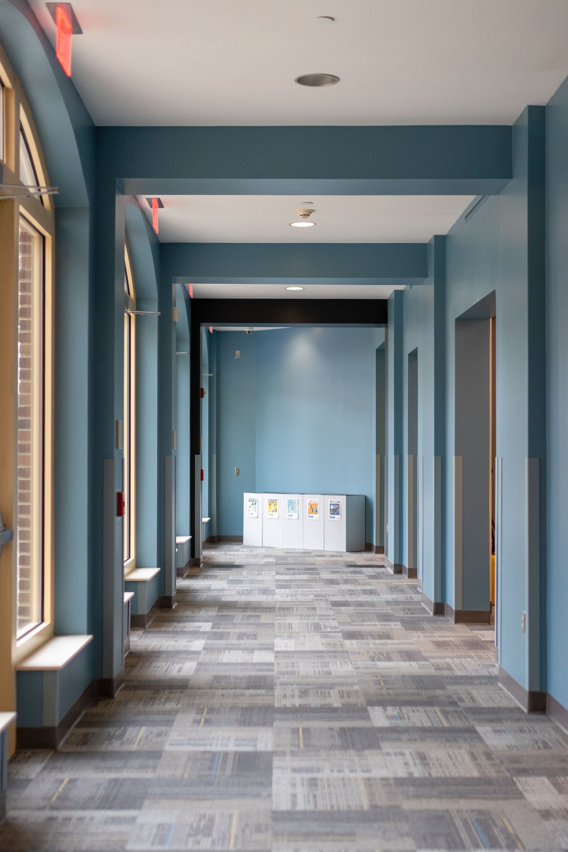 Eastview Terrace Kitchen's empty blue hallway with windows and patterned carpet in a building