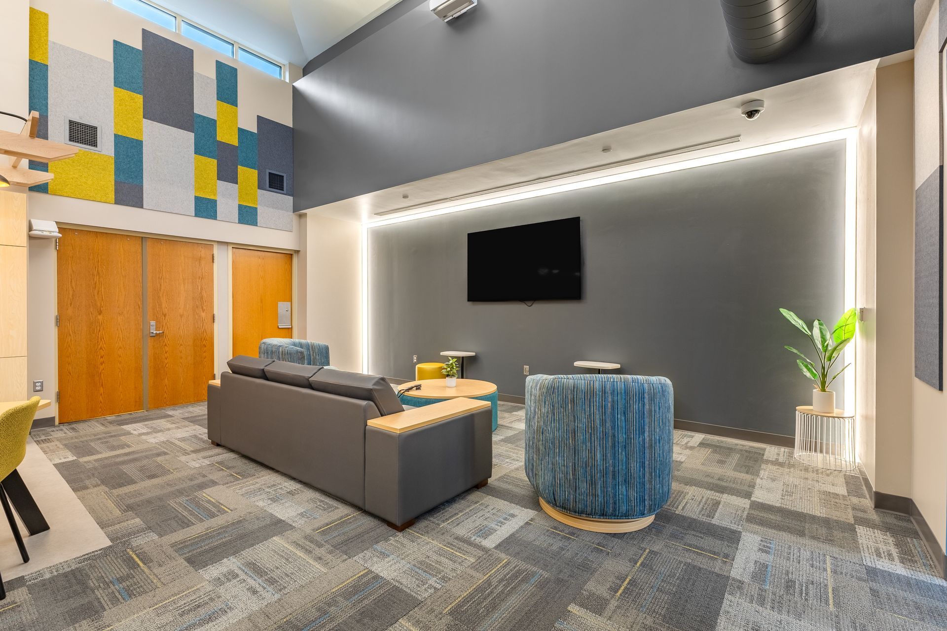 Eastview Terrace Kitchen's modern lobby lounge with gray sofa, blue ottoman, wall TV, wood doors, and geometric wall art