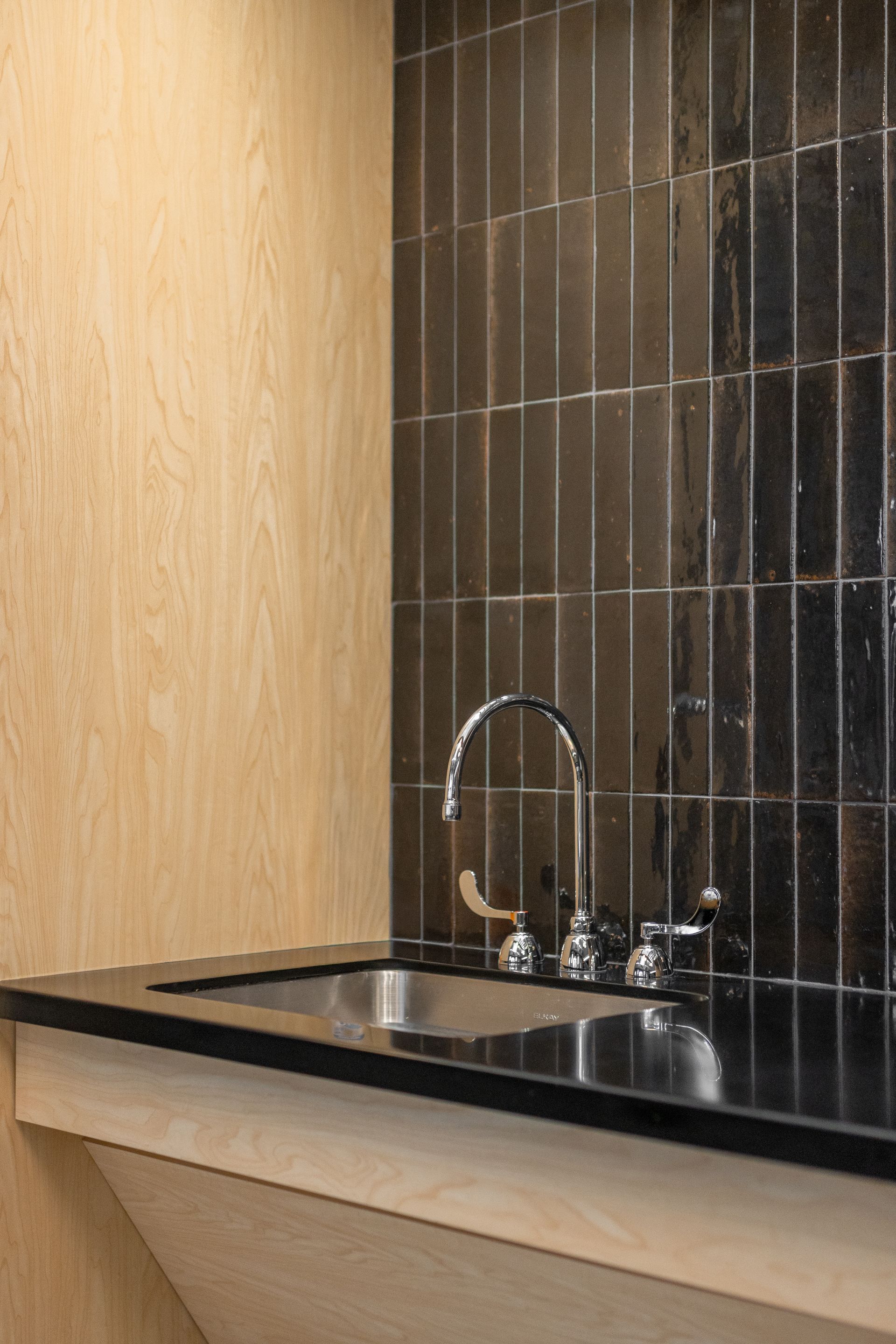 Eastview Terrace Kitchen's sink with chrome faucet, black countertop, and dark tiled backsplash