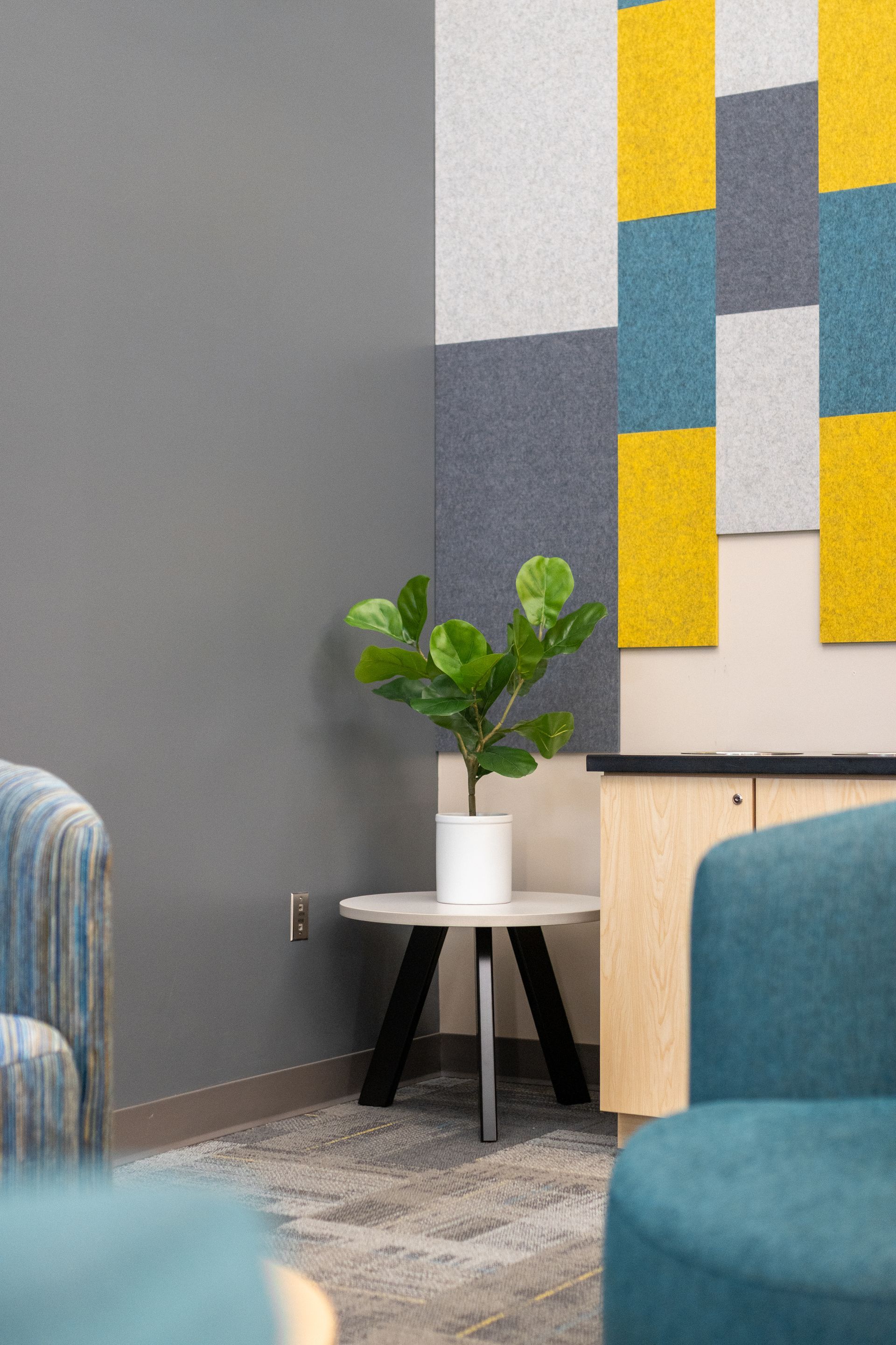 Eastview Terrace Kitchen's modern living room corner with teal chairs, a white side table, potted plant, and yellow-gray wall art