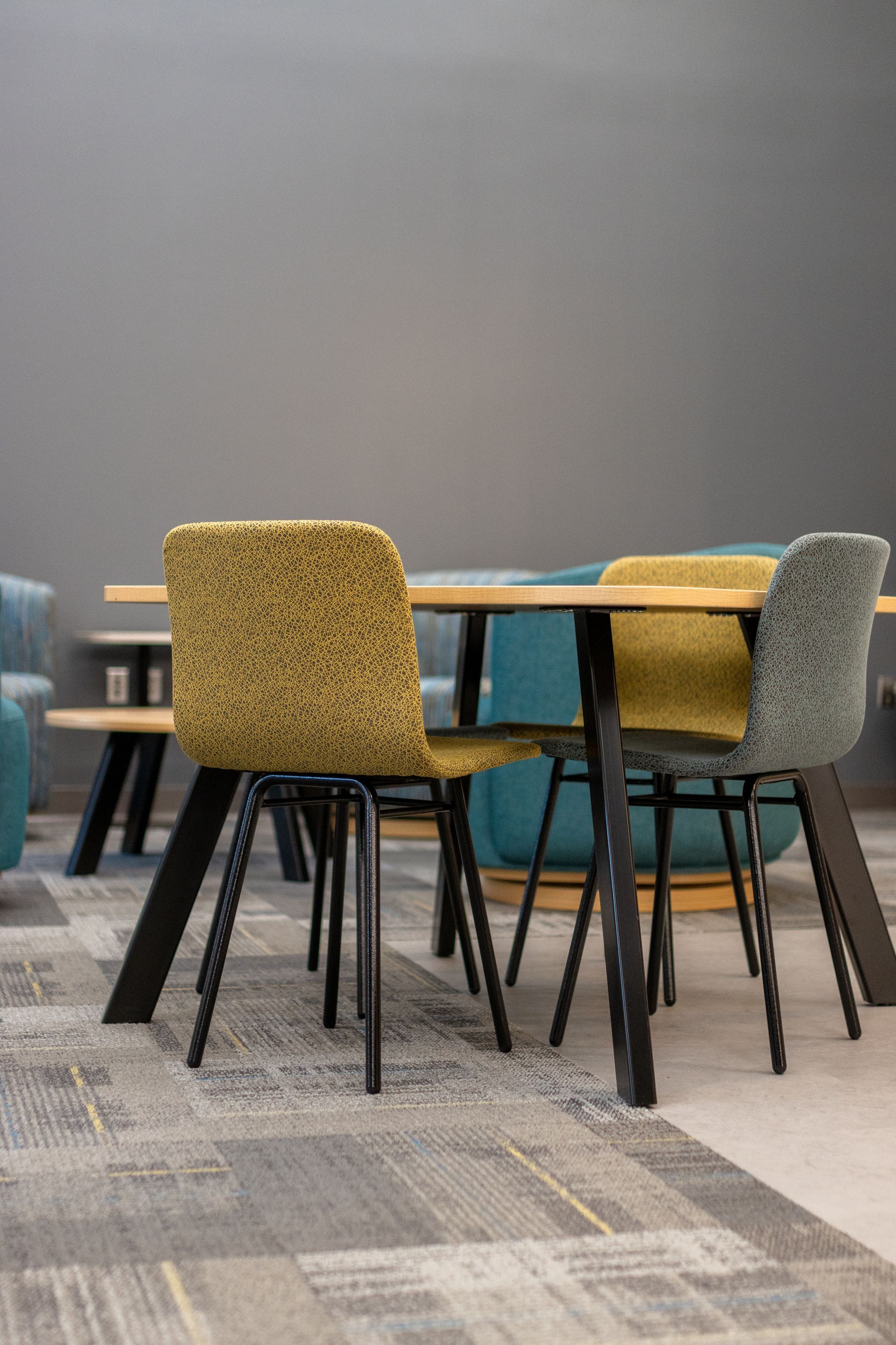 Eastview Terrace Kitchen's colorful chairs around a round table in a modern lounge with patterned carpet and gray wall.