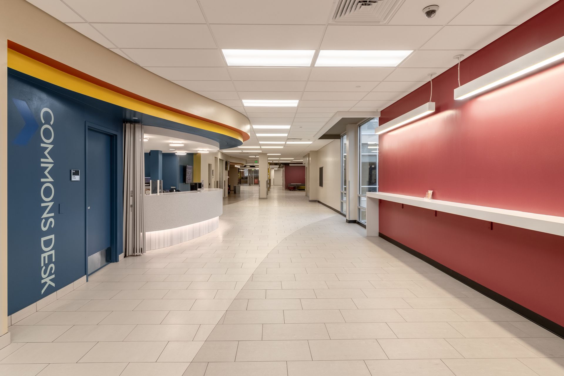 Hallway with red and blue walls, Commons Desk, and bright lighting.