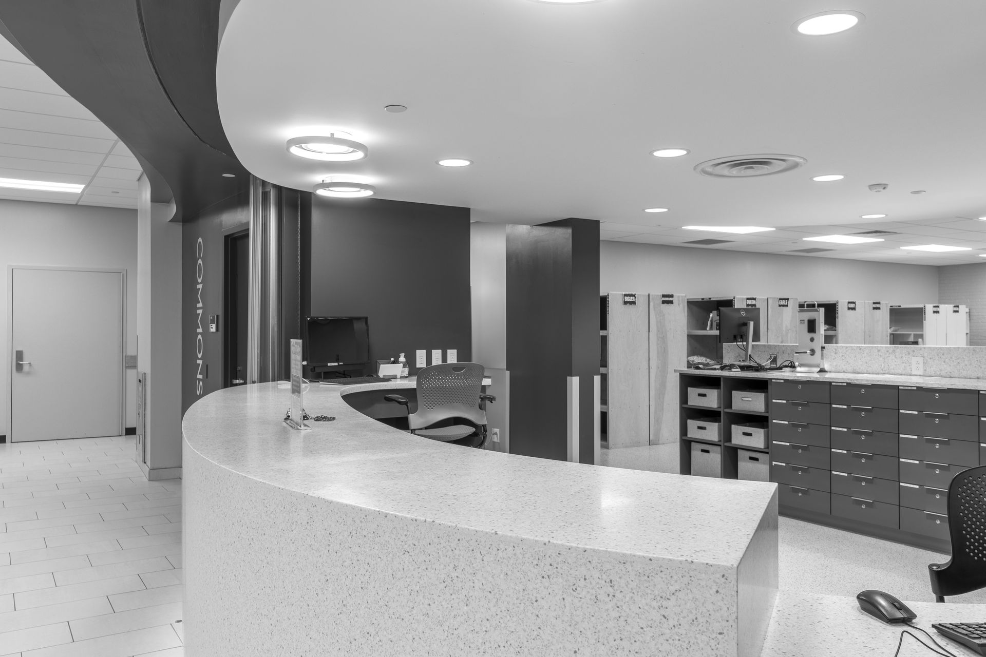 Monochrome view of a reception area with a curved countertop, computer, and storage cabinets.