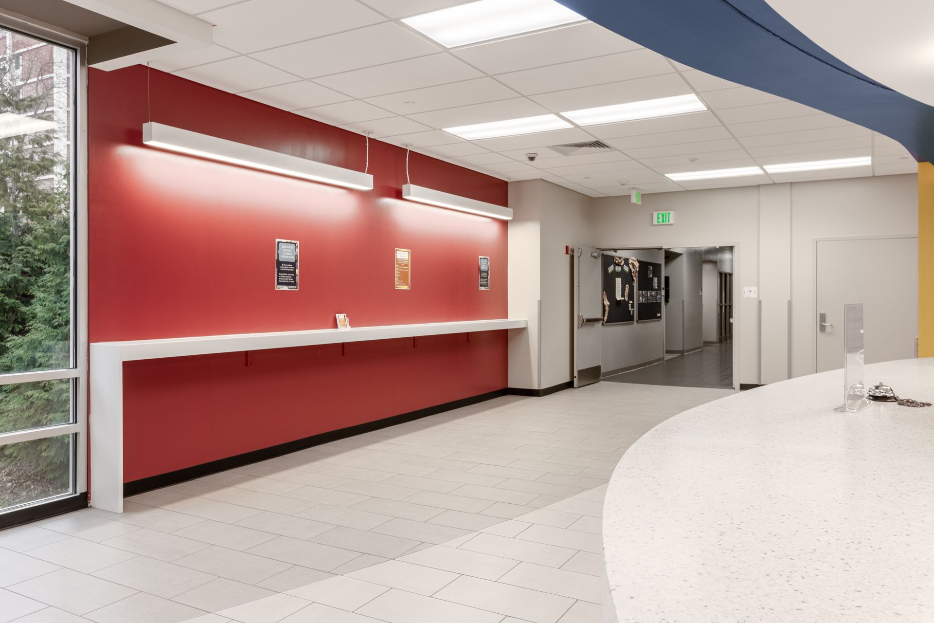Interior view of a modern hallway with a red accent wall, long white counter, and speckled floor.
