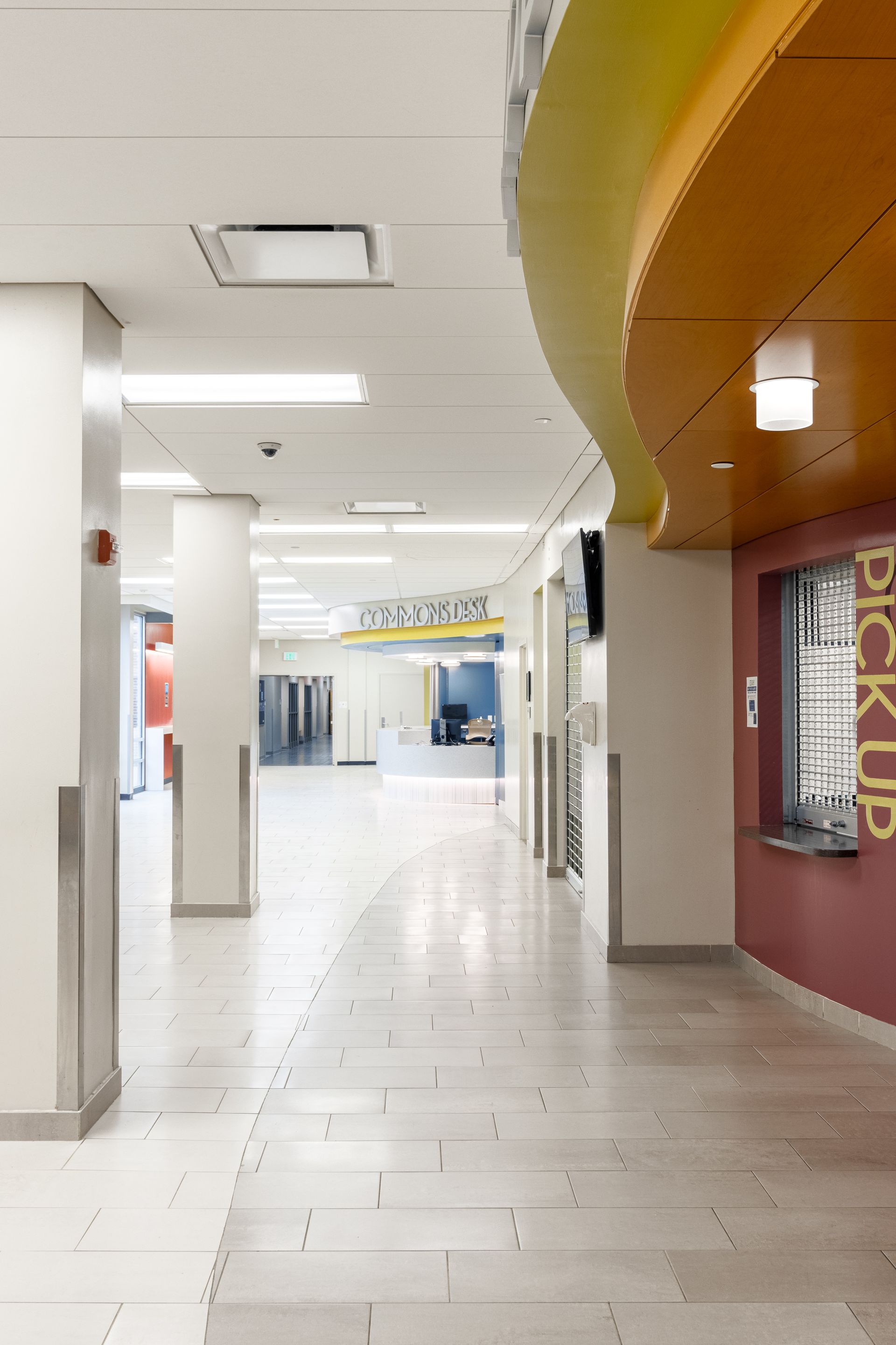 Hallway with white walls, gray floor, colorful ceiling accents, and a pick-up window.