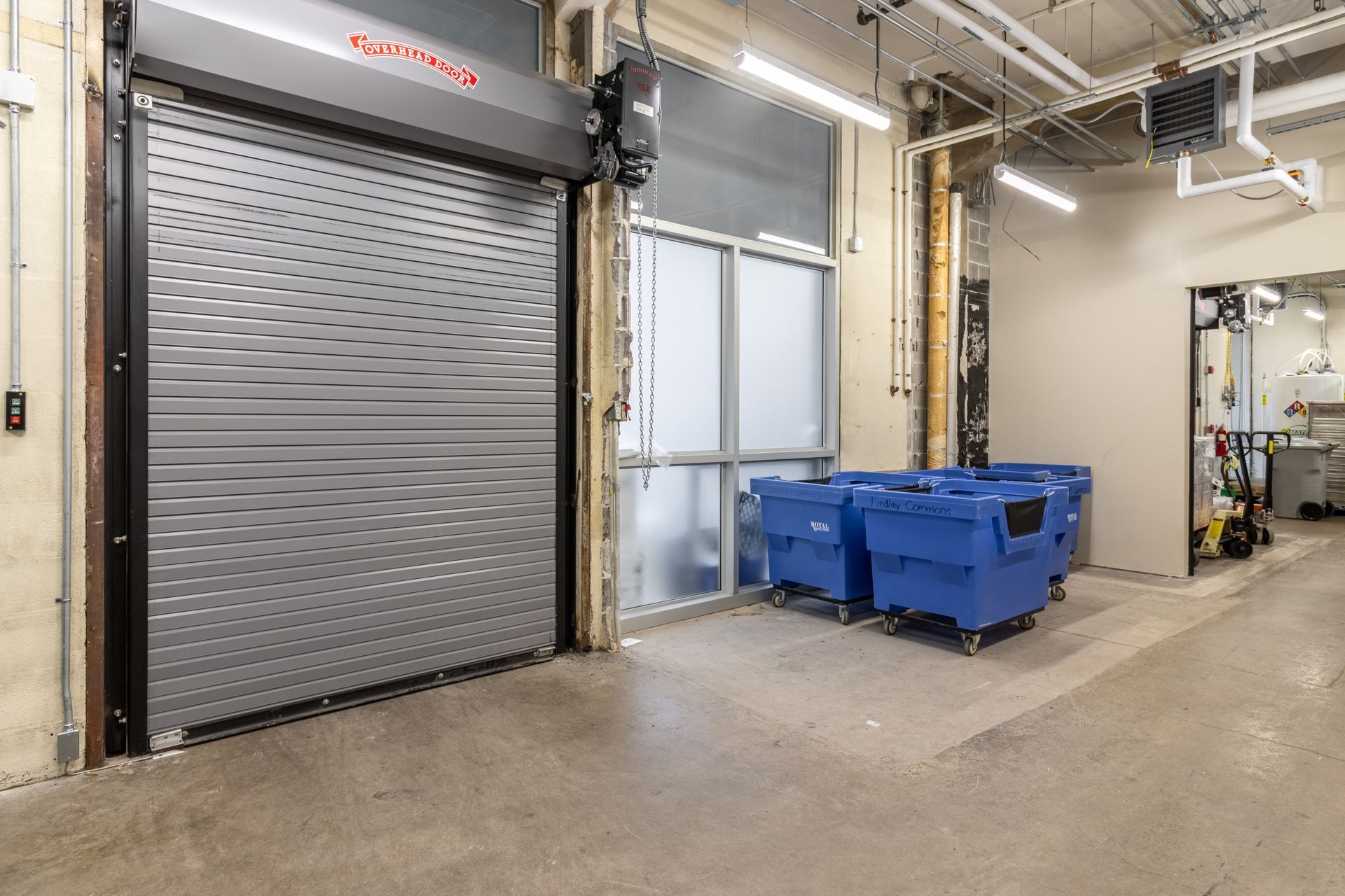 Rolling metal door open, with blue bins in front of an interior door and walkway.