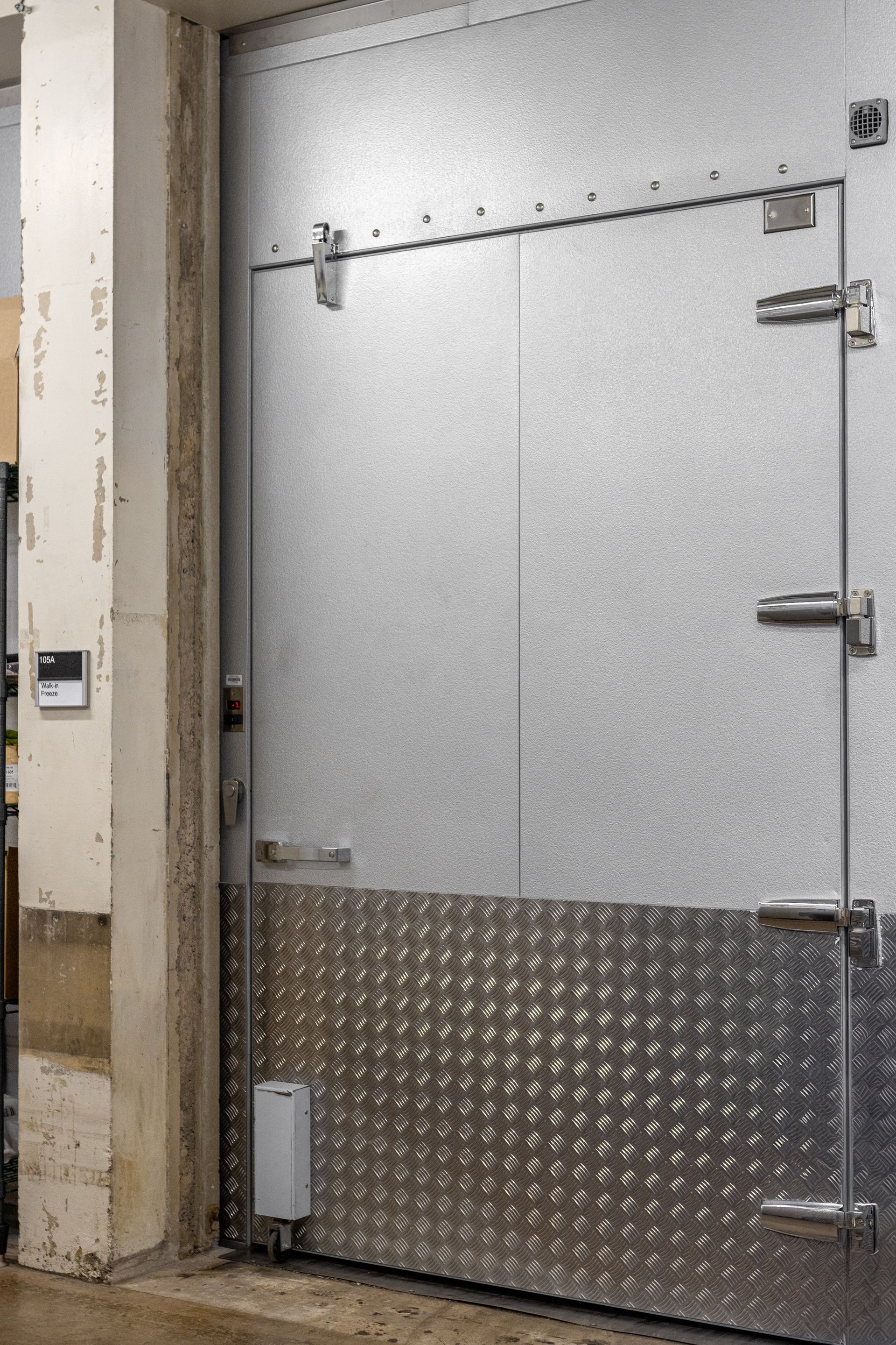 Large industrial metal door, partially open. The lower portion has a diamond plate finish.
