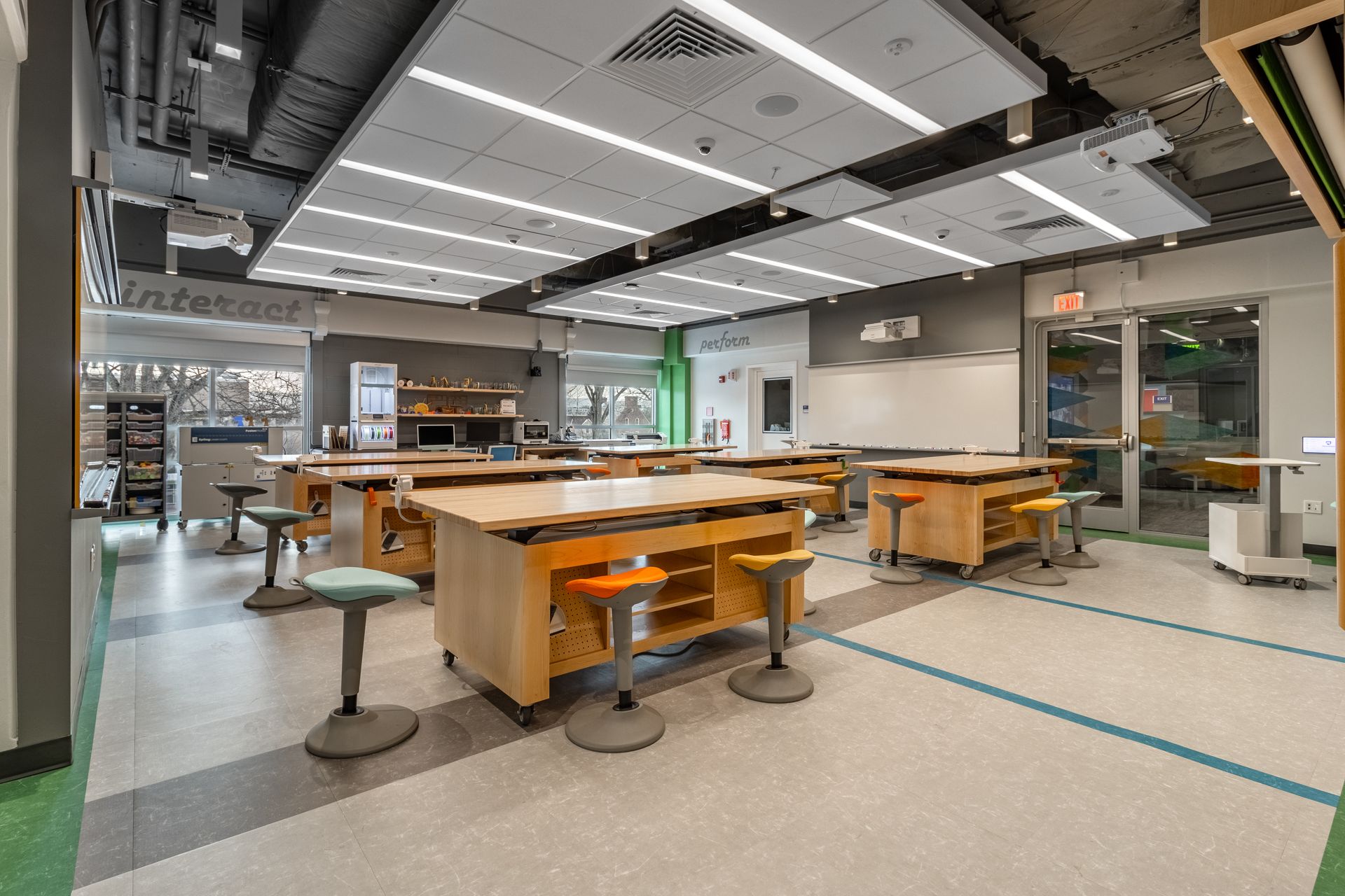 Modern classroom with work tables, stools, and open spaces, with a neutral and functional design.