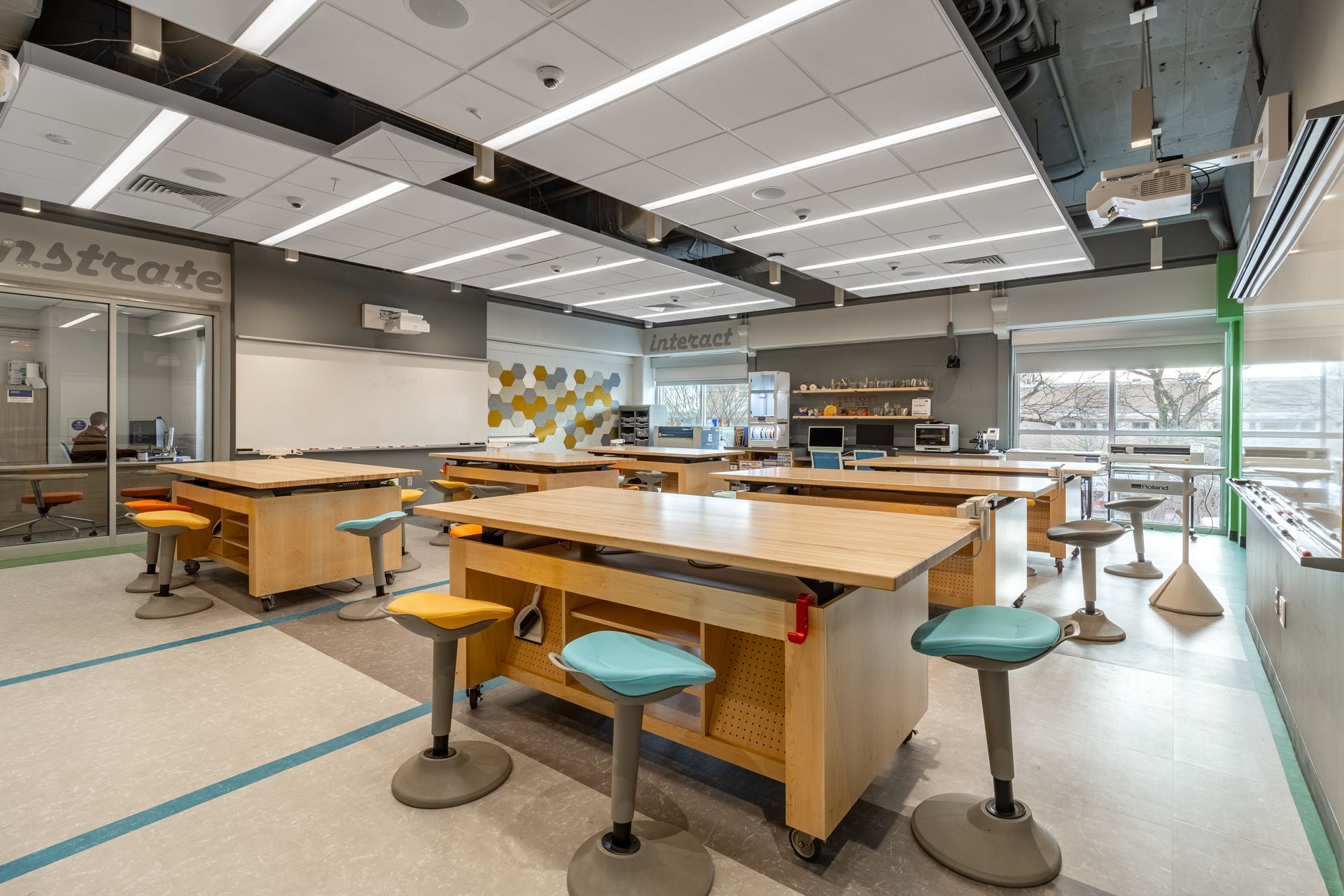 Art classroom with multiple work tables, stools, whiteboards, and computers.