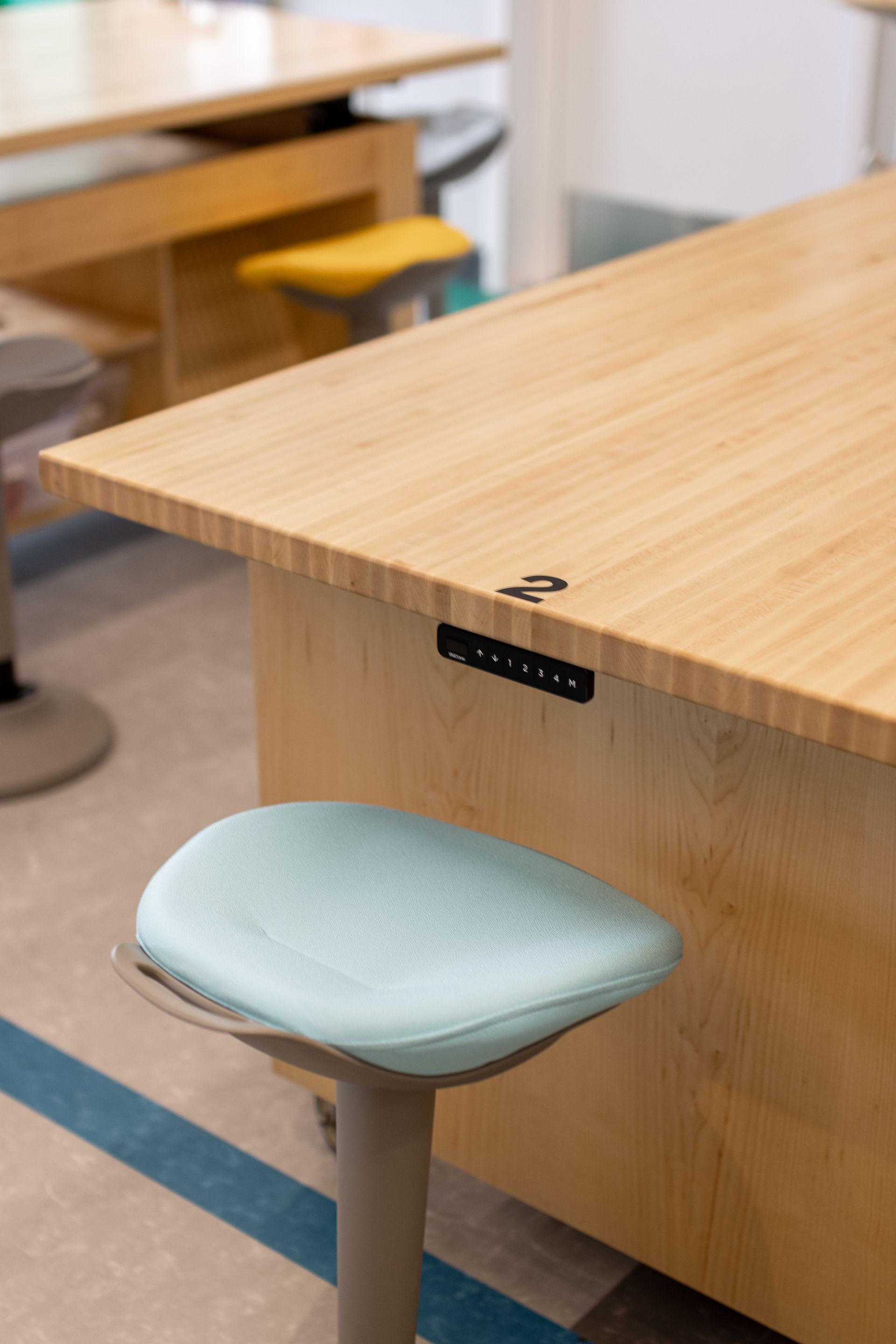 Light wood desks and a stool with a blue seat in a classroom setting.