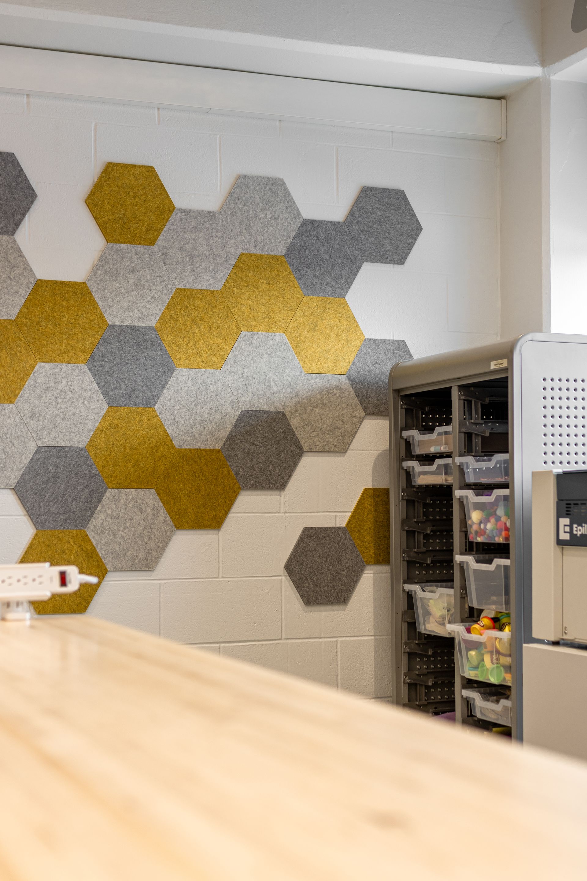 Honeycomb-patterned wall decor with gold and gray hexagons on a white brick wall, next to a storage cabinet.